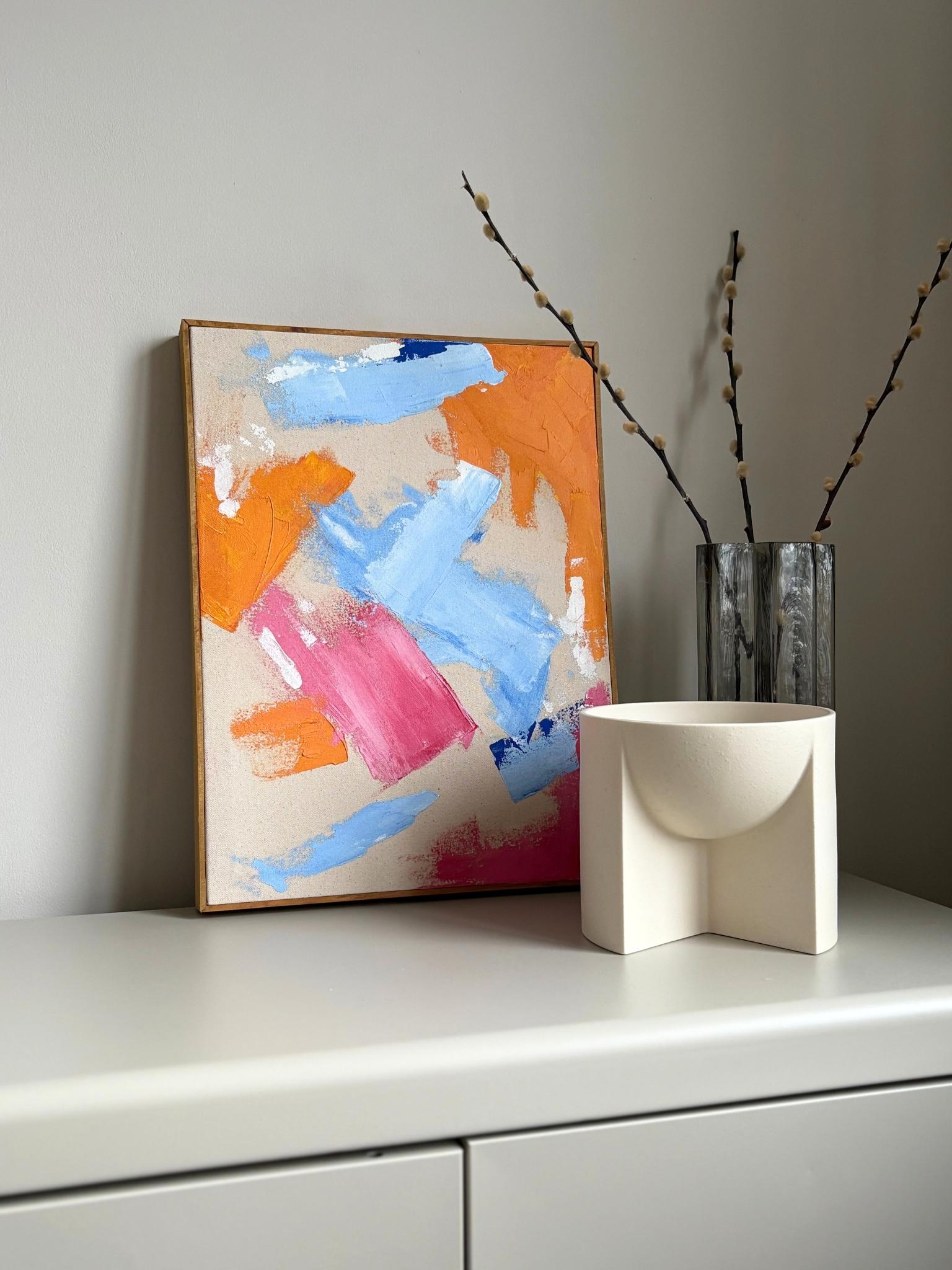 Finished framed abstract canvas artwork created using Plan’s Mix (primary colours) palette, featuring expressive brushstrokes in blue, orange and pink on raw canvas, styled on a minimalist shelf in a modern home interior.