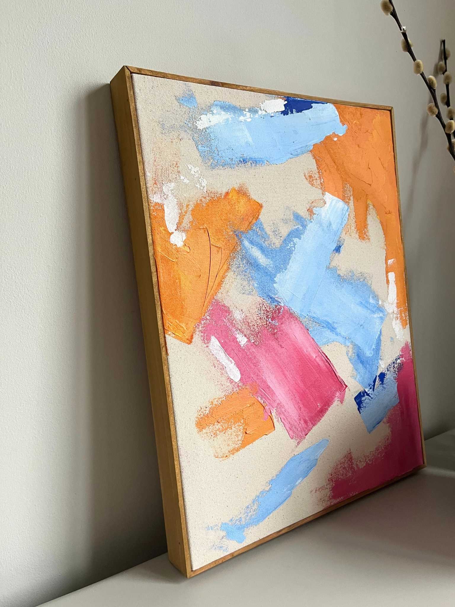 Finished framed abstract canvas artwork created using Plan’s Mix (primary colours) palette, featuring expressive brushstrokes in blue, orange and pink on raw canvas, styled on a minimalist shelf in a modern home interior.
