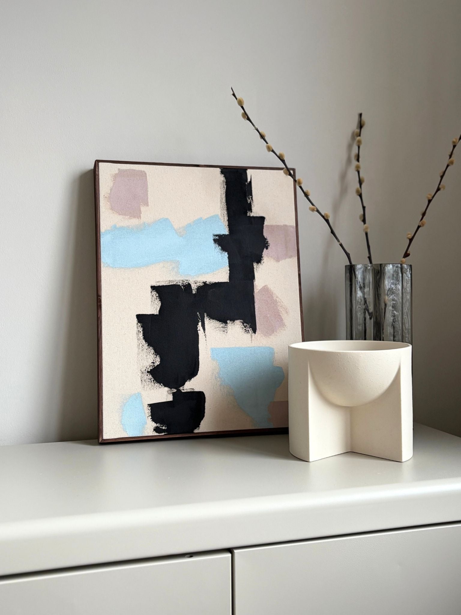 Finished framed abstract artwork made with Plan’s Mix primary colours palette, combining bold black marks with soft blue and muted pastel tones on raw canvas, photographed as modern wall art in a calm, neutral interior setting.