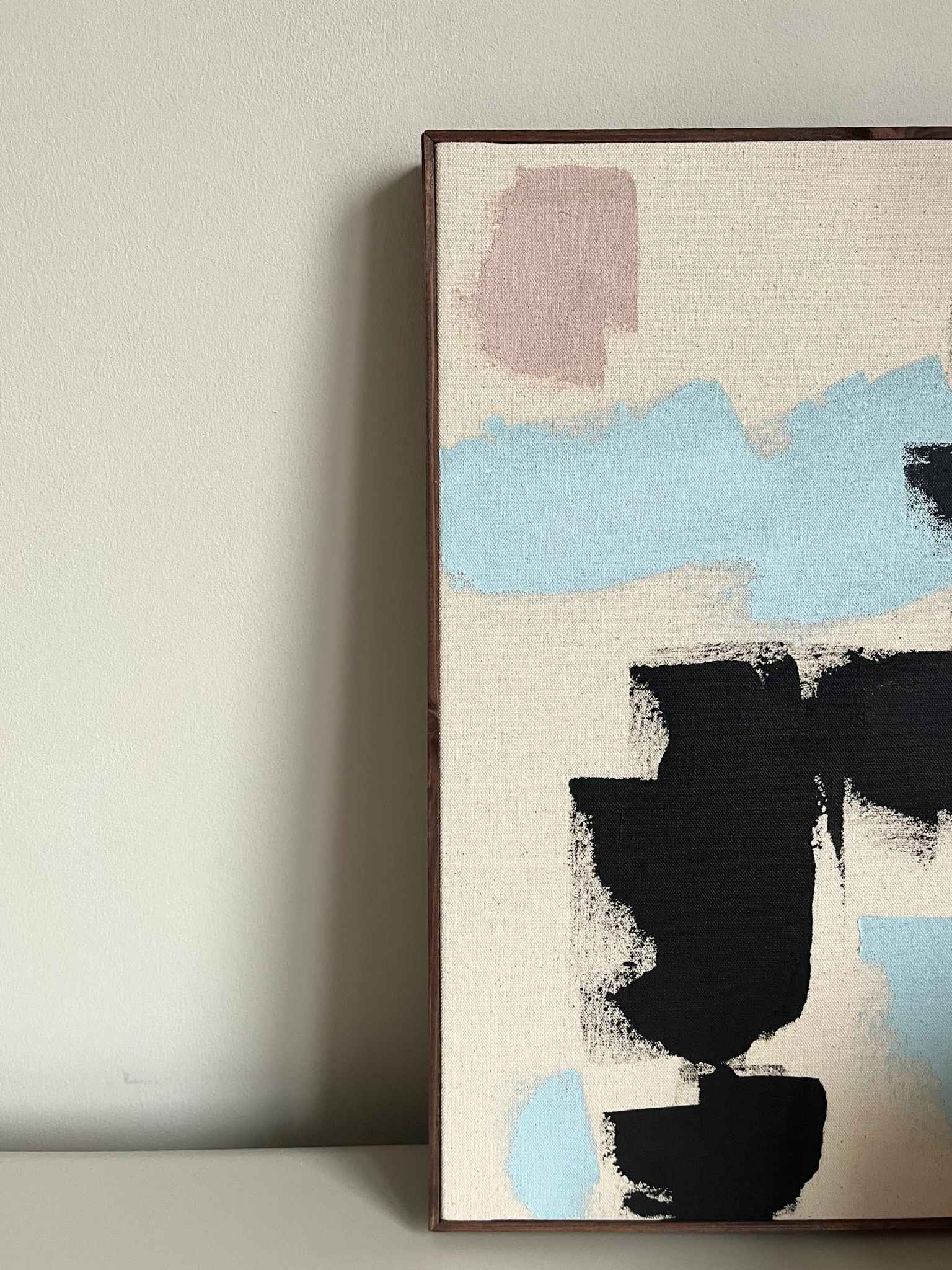 Finished framed abstract artwork made with Plan’s Mix primary colours palette, combining bold black marks with soft blue and muted pastel tones on raw canvas, photographed as modern wall art in a calm, neutral interior setting.