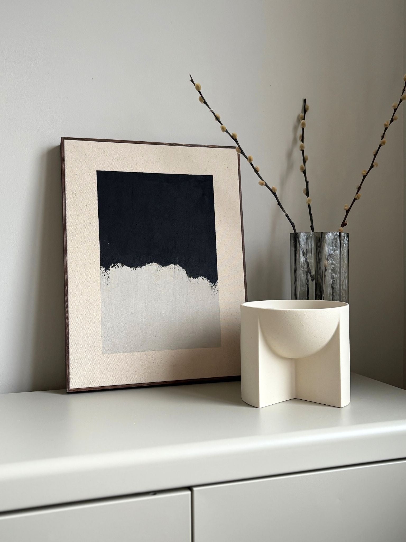 Finished framed monochrome abstract artwork on cotton canvas with dark oak edge frame, created using Plan’s monochrome cotton palette with layered black and white brushstrokes, styled on a shelf in a modern interior.