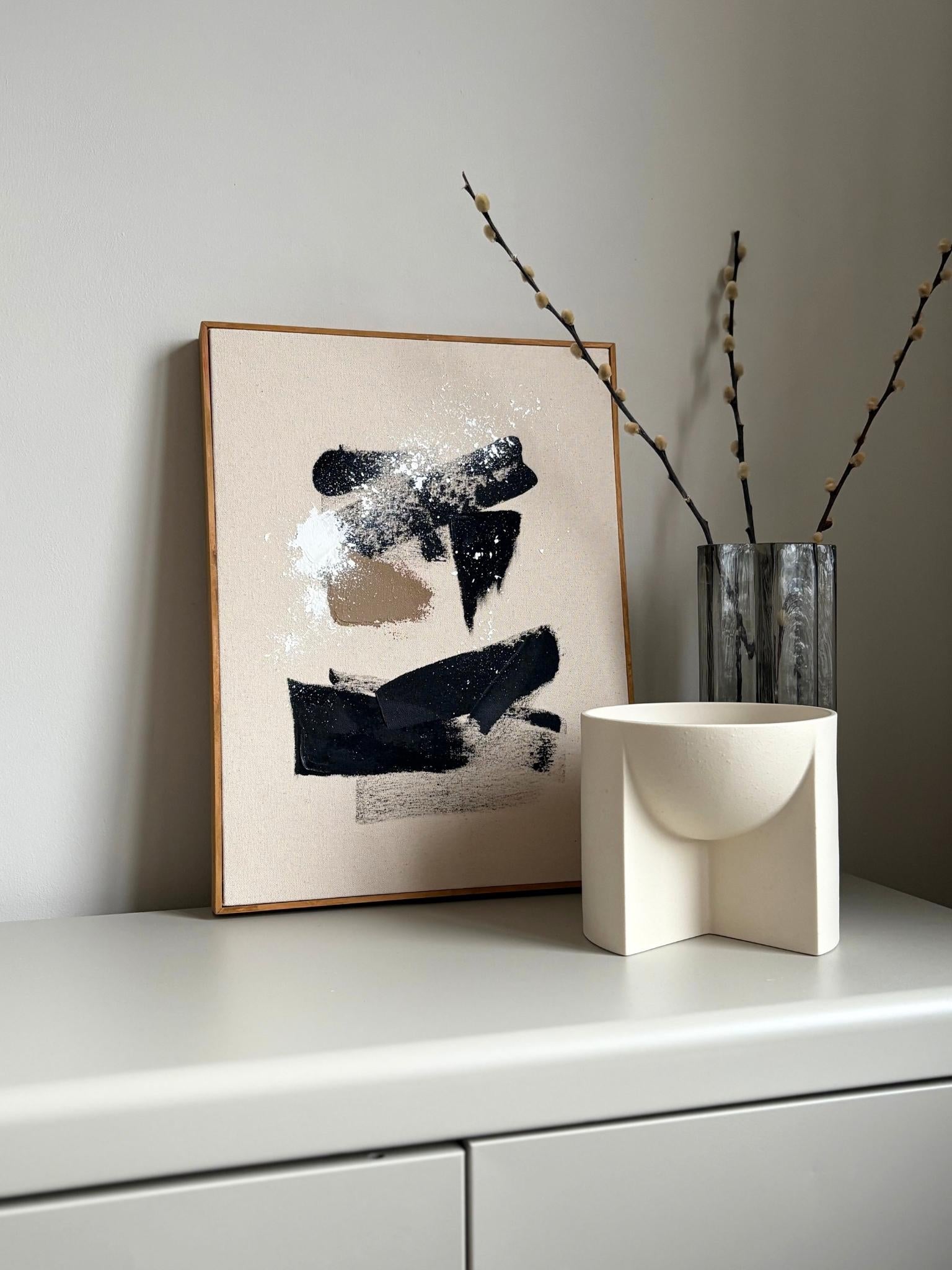Finished framed abstract canvas artwork made with Plan’s monochrome cotton palette, featuring a bold black cross-like form, white and beige marks, and soft neutral background, photographed as contemporary wall art.
