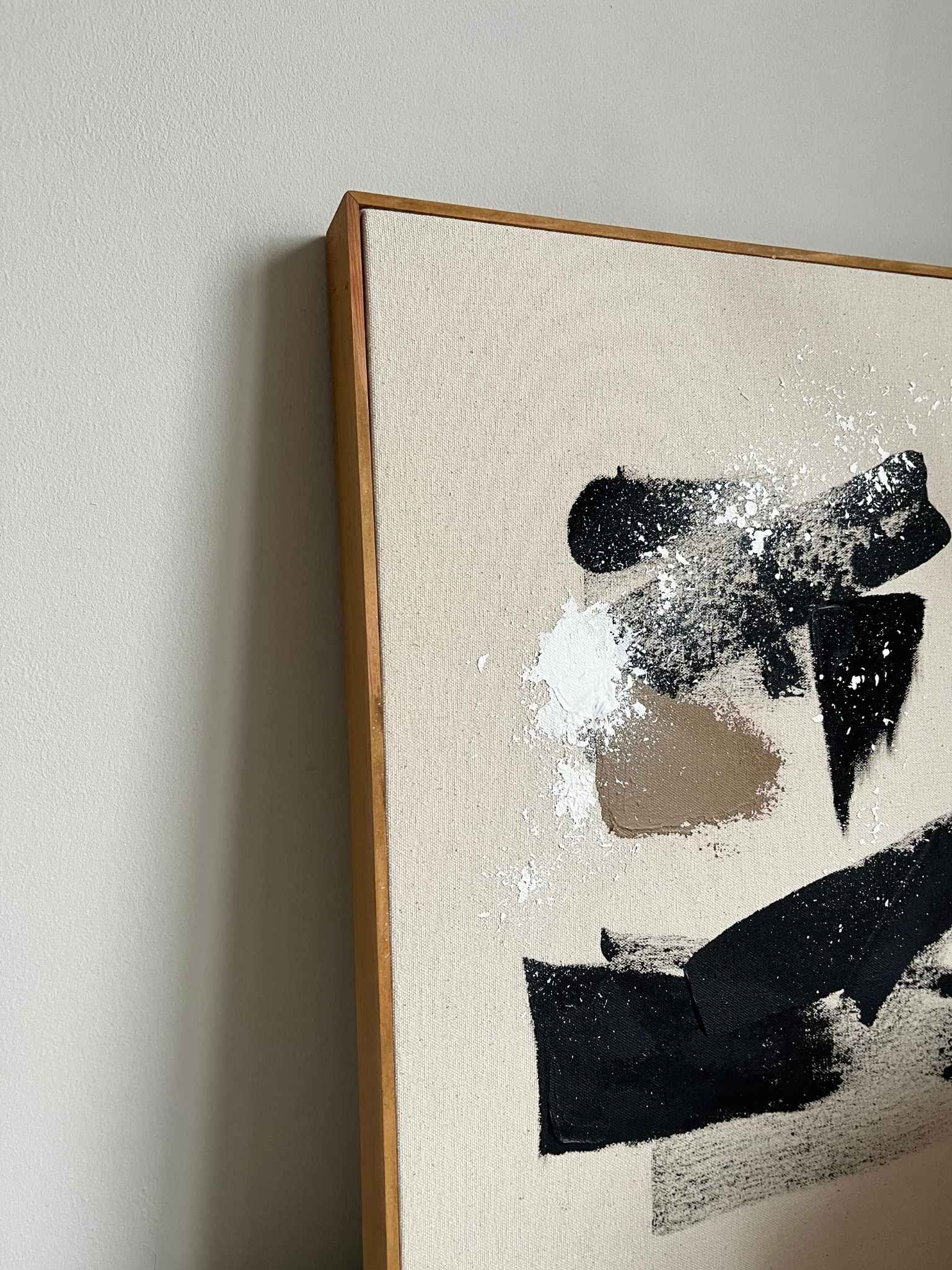 Finished framed abstract canvas artwork made with Plan’s monochrome cotton palette, featuring a bold black cross-like form, white and beige marks, and soft neutral background, photographed as contemporary wall art.