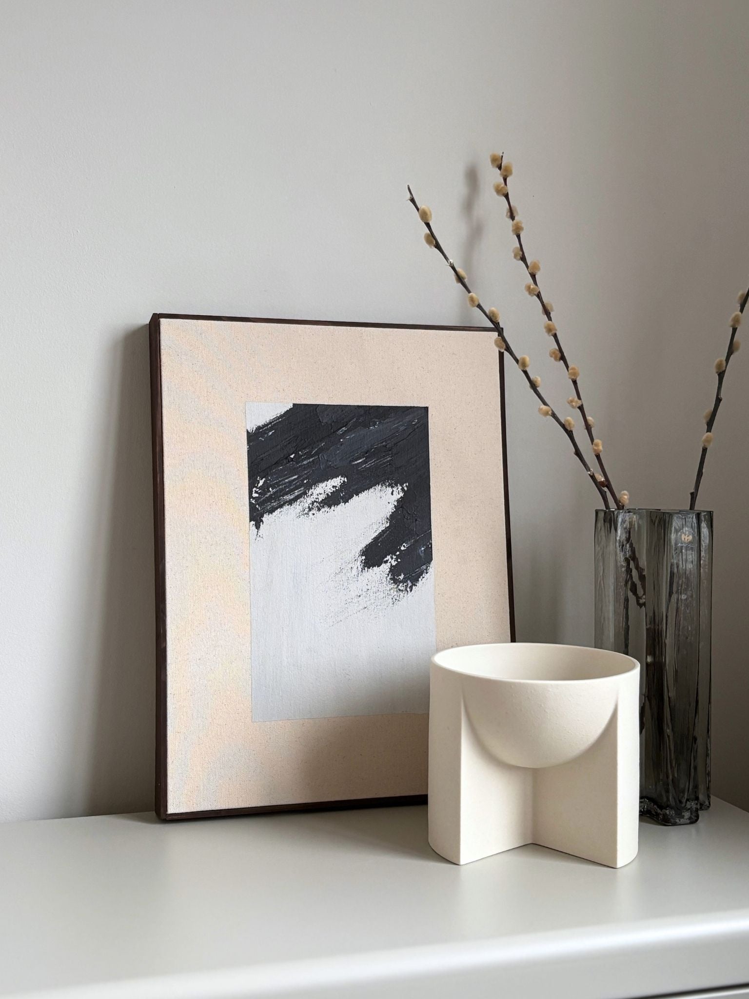 Finished framed canvas artwork in monochrome tones, featuring expressive black brush marks on natural cotton canvas, styled on a sideboard with sculptural décor.