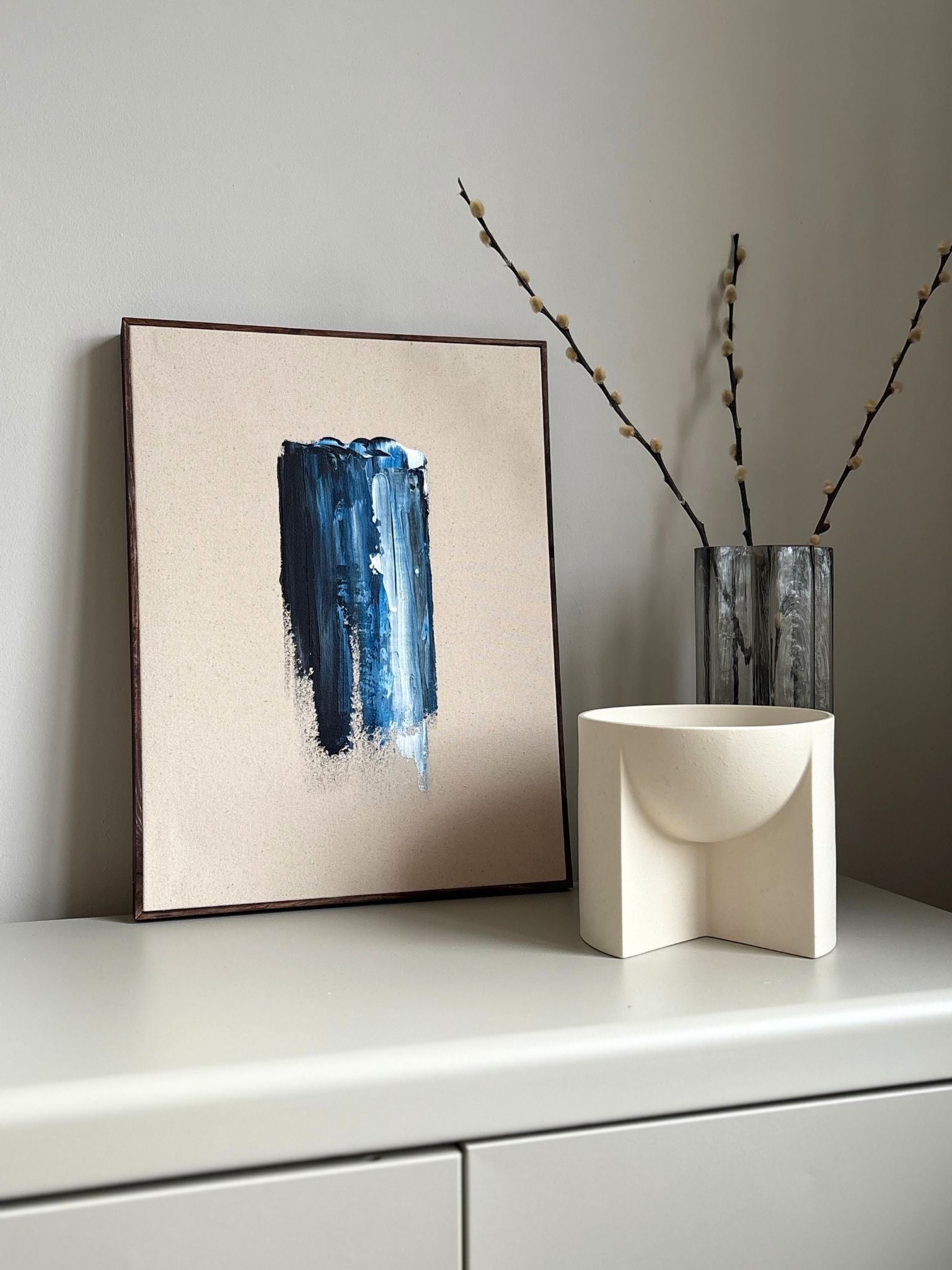 Finished framed abstract canvas artwork created with Plan’s Navy & Bright palette, featuring a bold vertical navy brushstroke on raw canvas with dark oak edge frame, styled on a minimalist surface with sculptural decor.