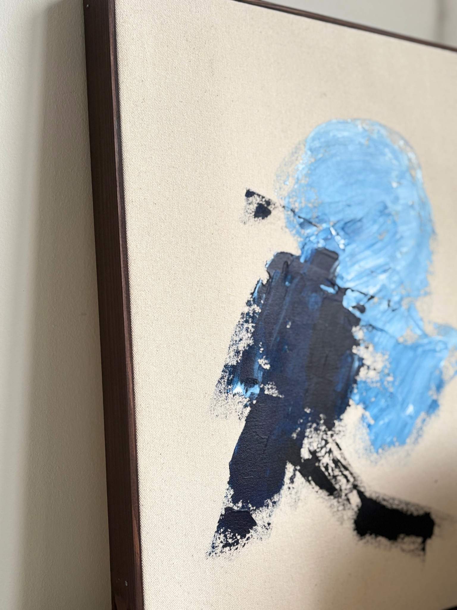 Finished framed canvas artwork with expressive navy and soft blue brushwork on natural canvas, styled on a sideboard in a minimalist interior.