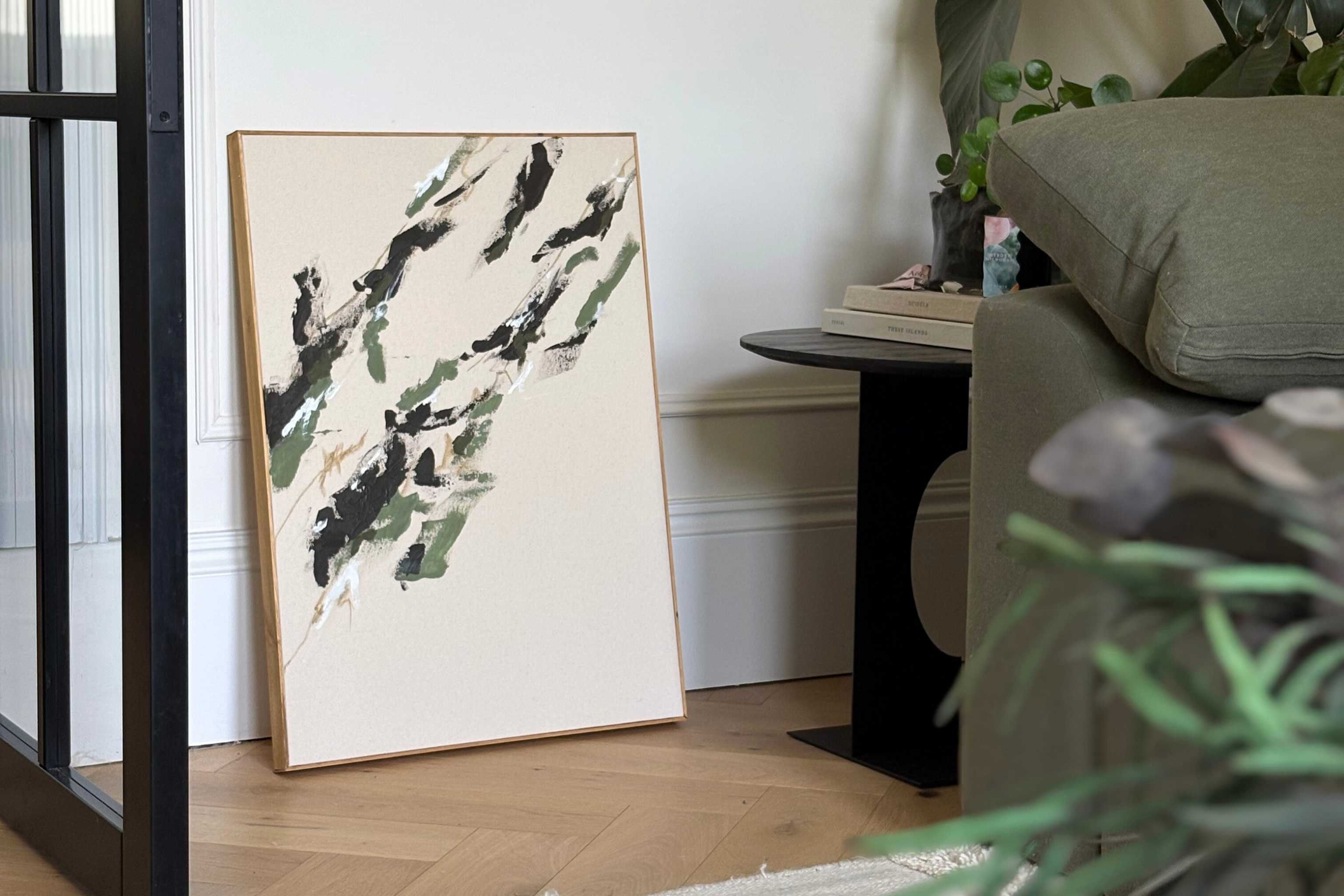 Framed abstract canvas artwork created with a Plan art kit, leaning against a wall in a modern living space, showing a finished piece designed to suit a considered home interior