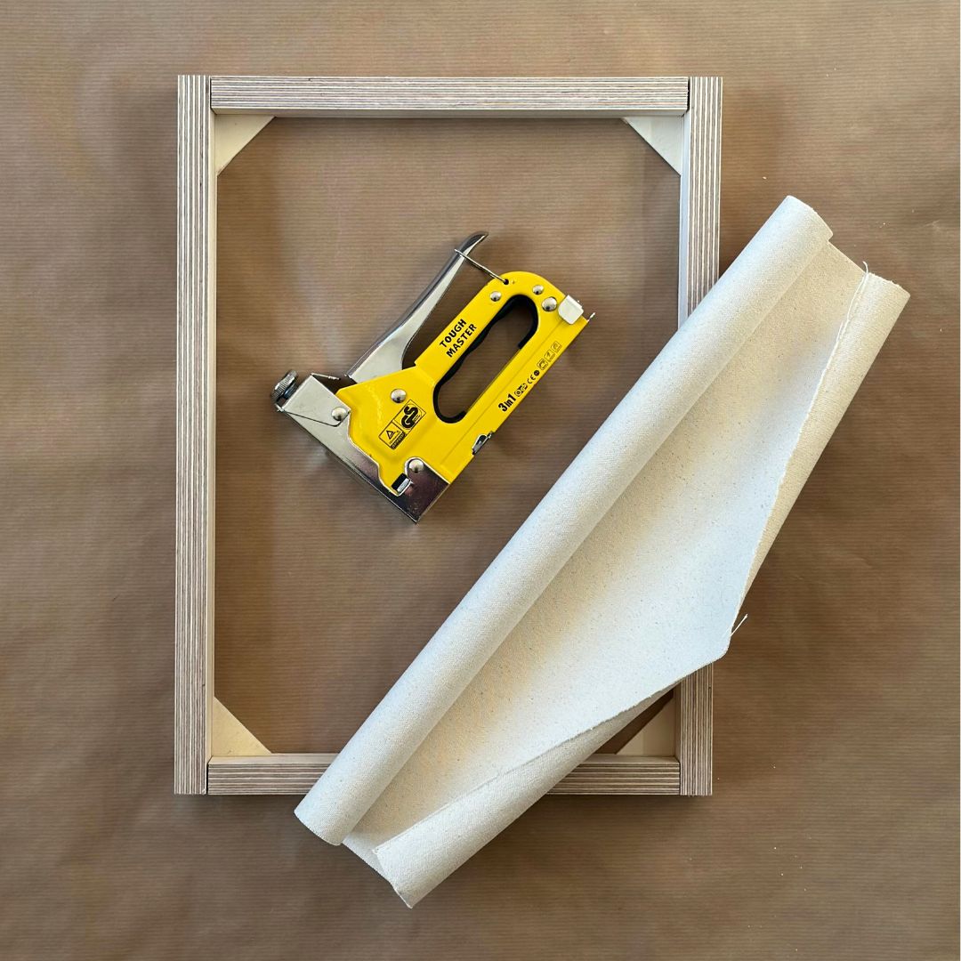 Stretching raw cotton or linen canvas onto a custom wooden frame using a staple gun as part of a DIY framed canvas art kit.