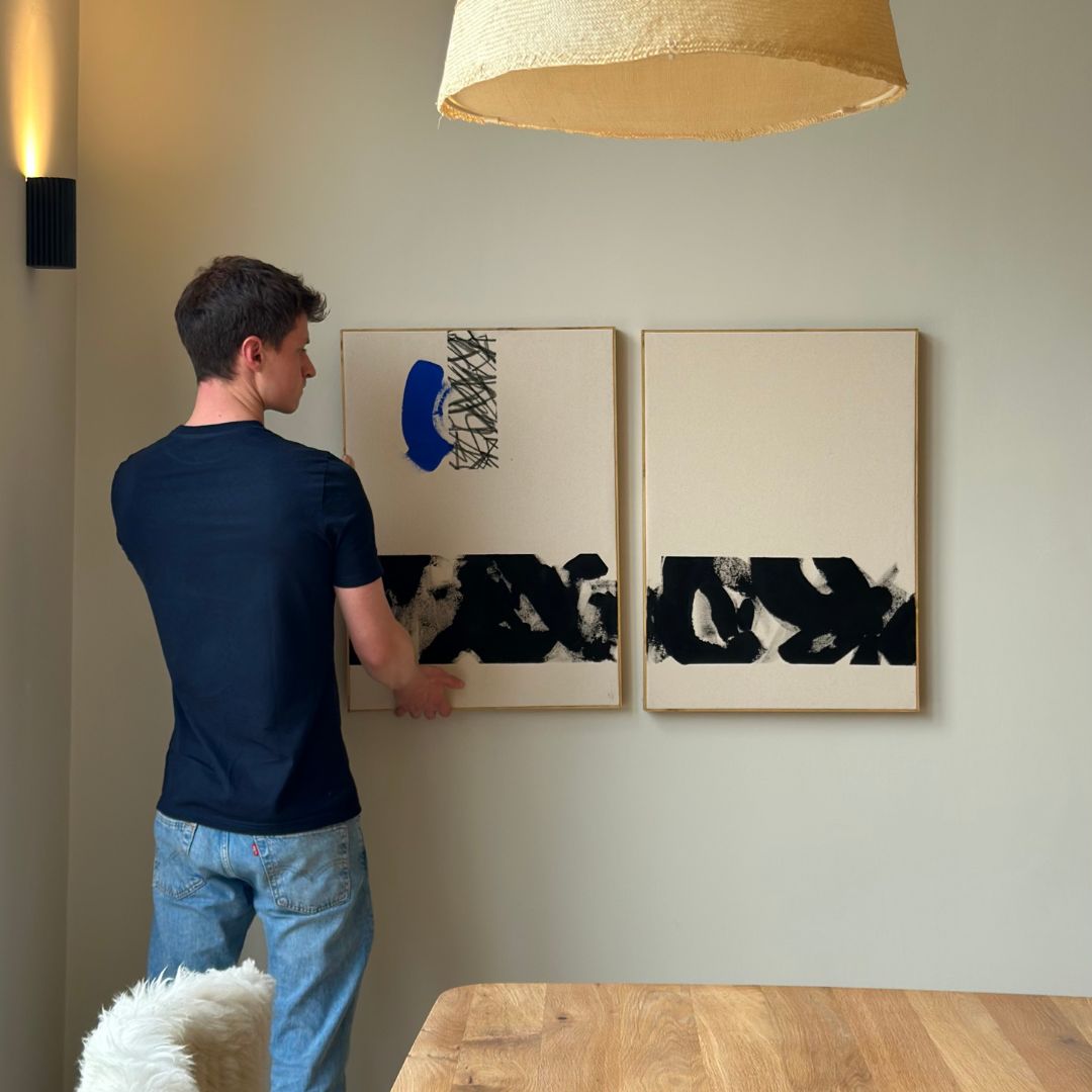 Person hanging a framed canvas artwork created with a DIY art kit in a Scandinavian style home interior setting.