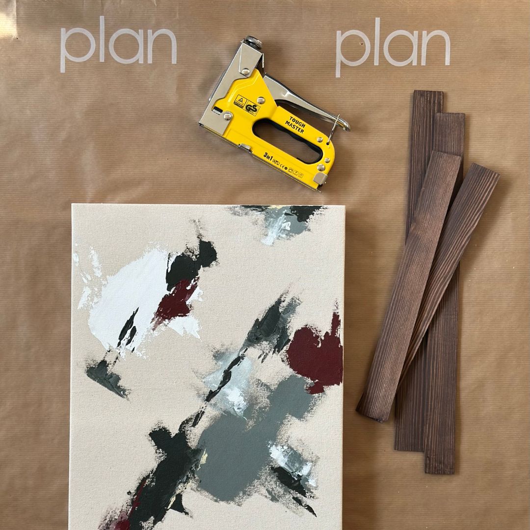 Wooden edge frame pieces with staple gun and finished artwork used to frame a canvas as part of a DIY art kit process.