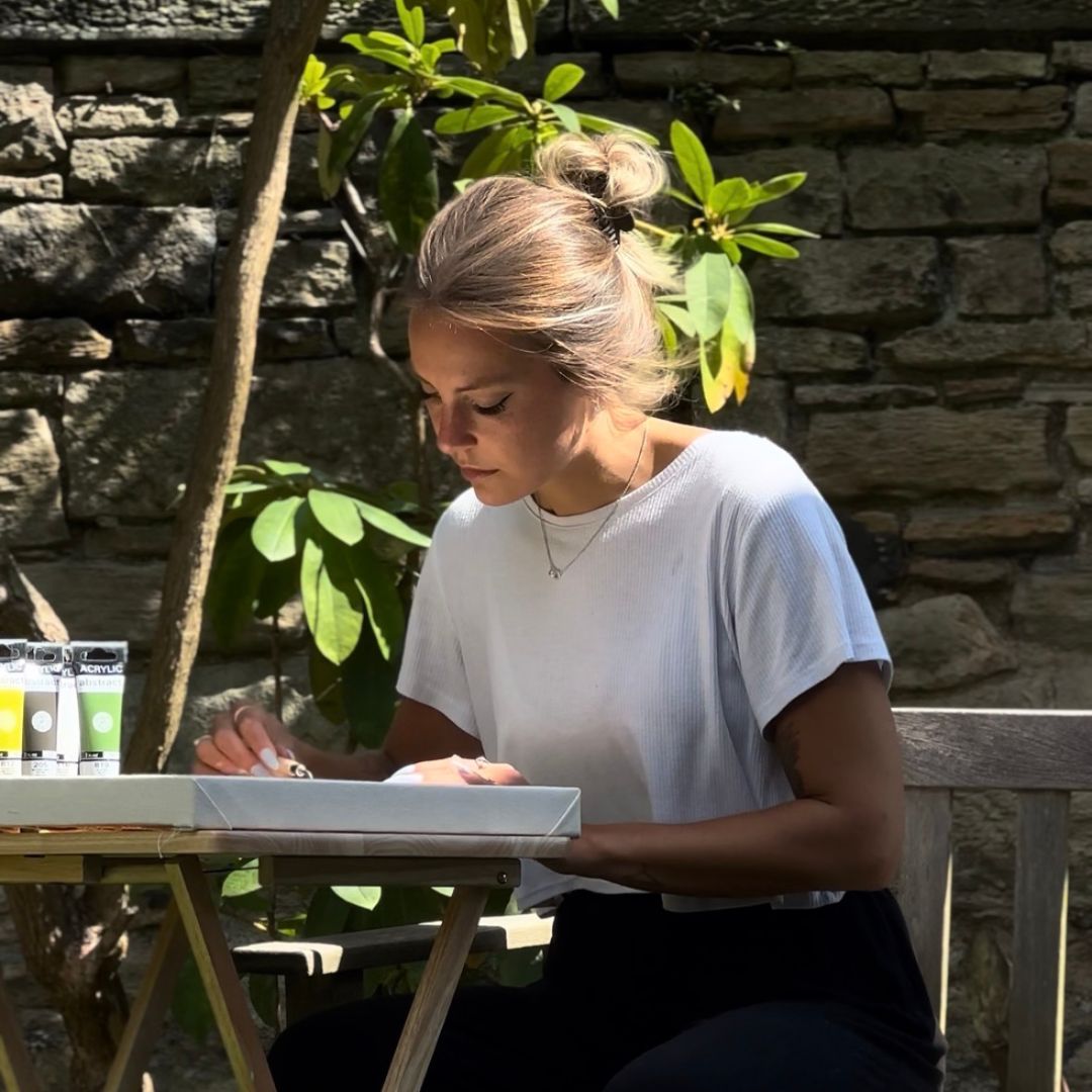Person painting a canvas artwork outdoors as part of a relaxed, hands-on DIY art kit experience.