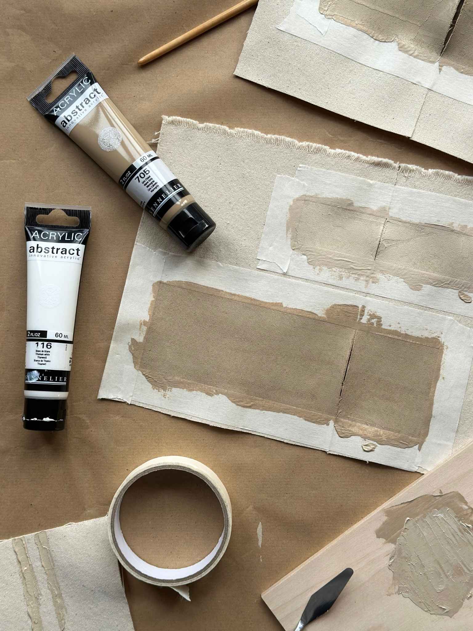 Paint tubes and canvas practice pieces from a Plan art kit laid out on a table, showing how to test colours and techniques before painting the main artwork