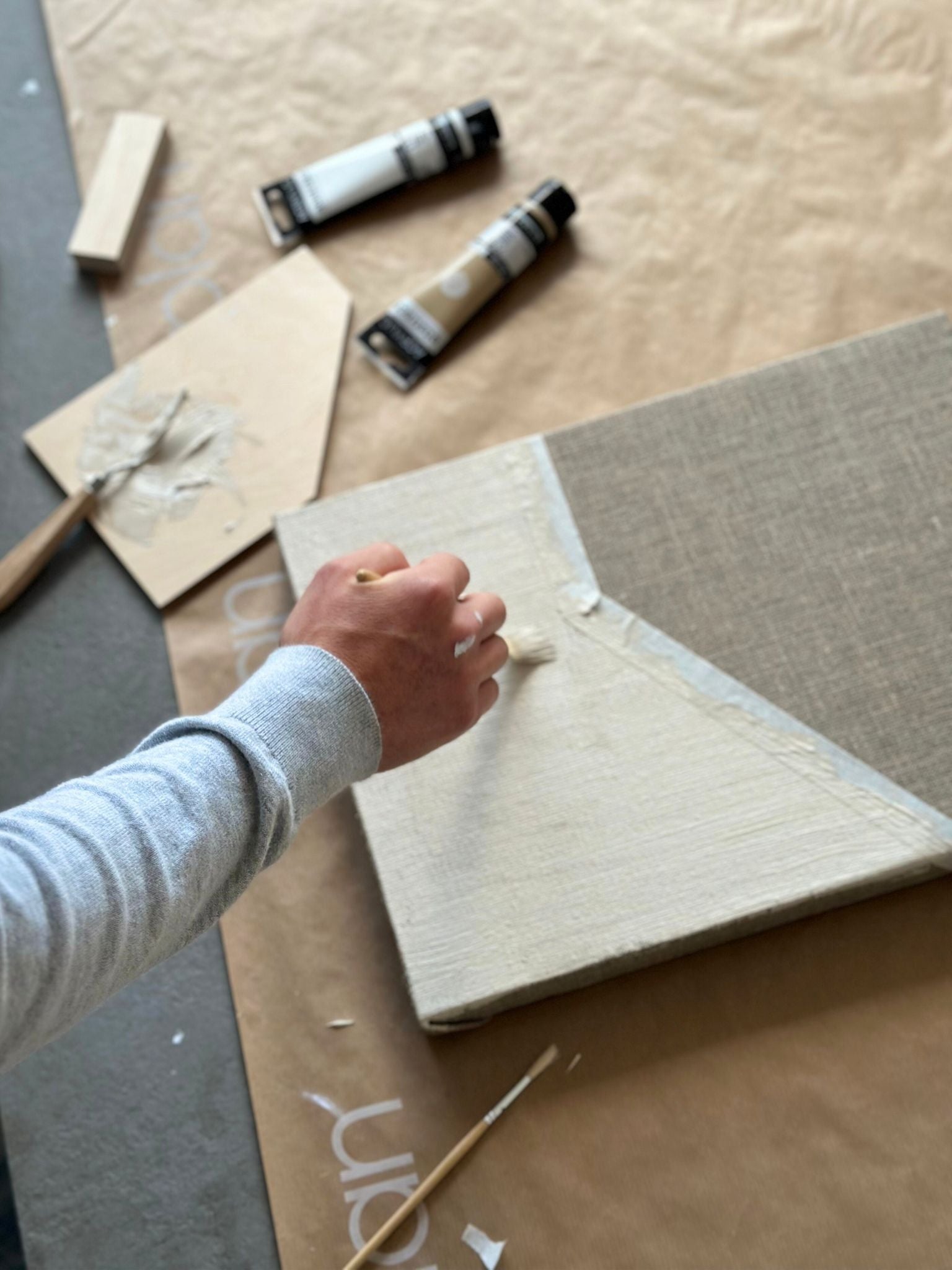 Close-up of paint being applied to a linen canvas using a Plan DIY framed canvas art kit, with art tools and paints close by.