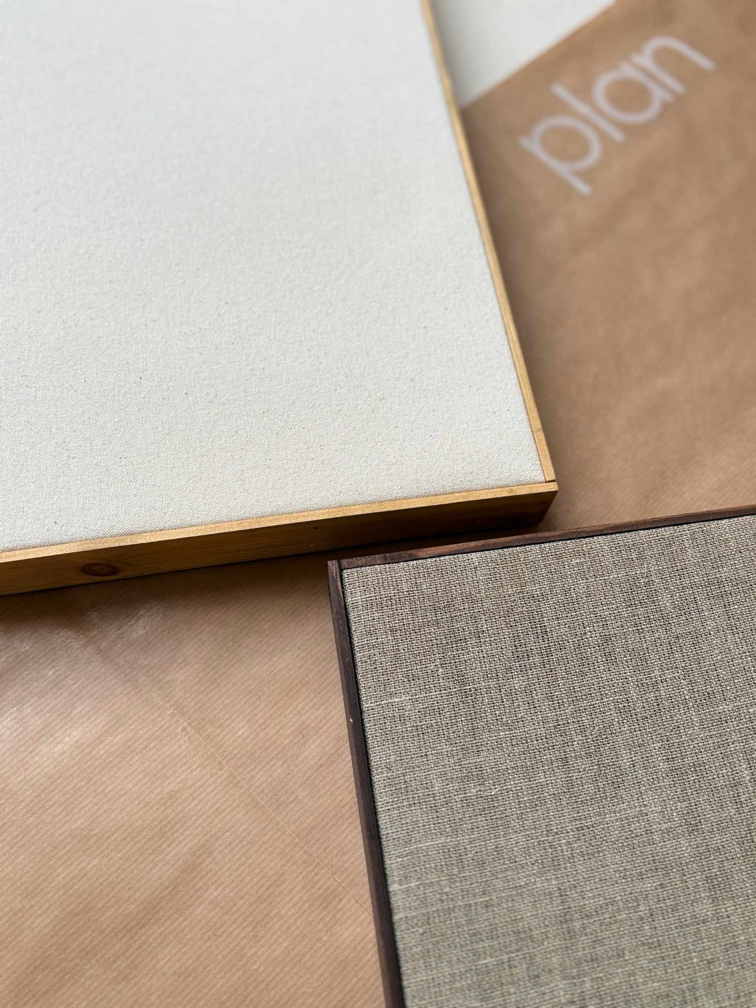 Close-up of two blank framed canvases from a DIY framed canvas art kit, showing natural cotton and linen canvas textures with handcrafted oak and dark oak edge frames on a studio work surface