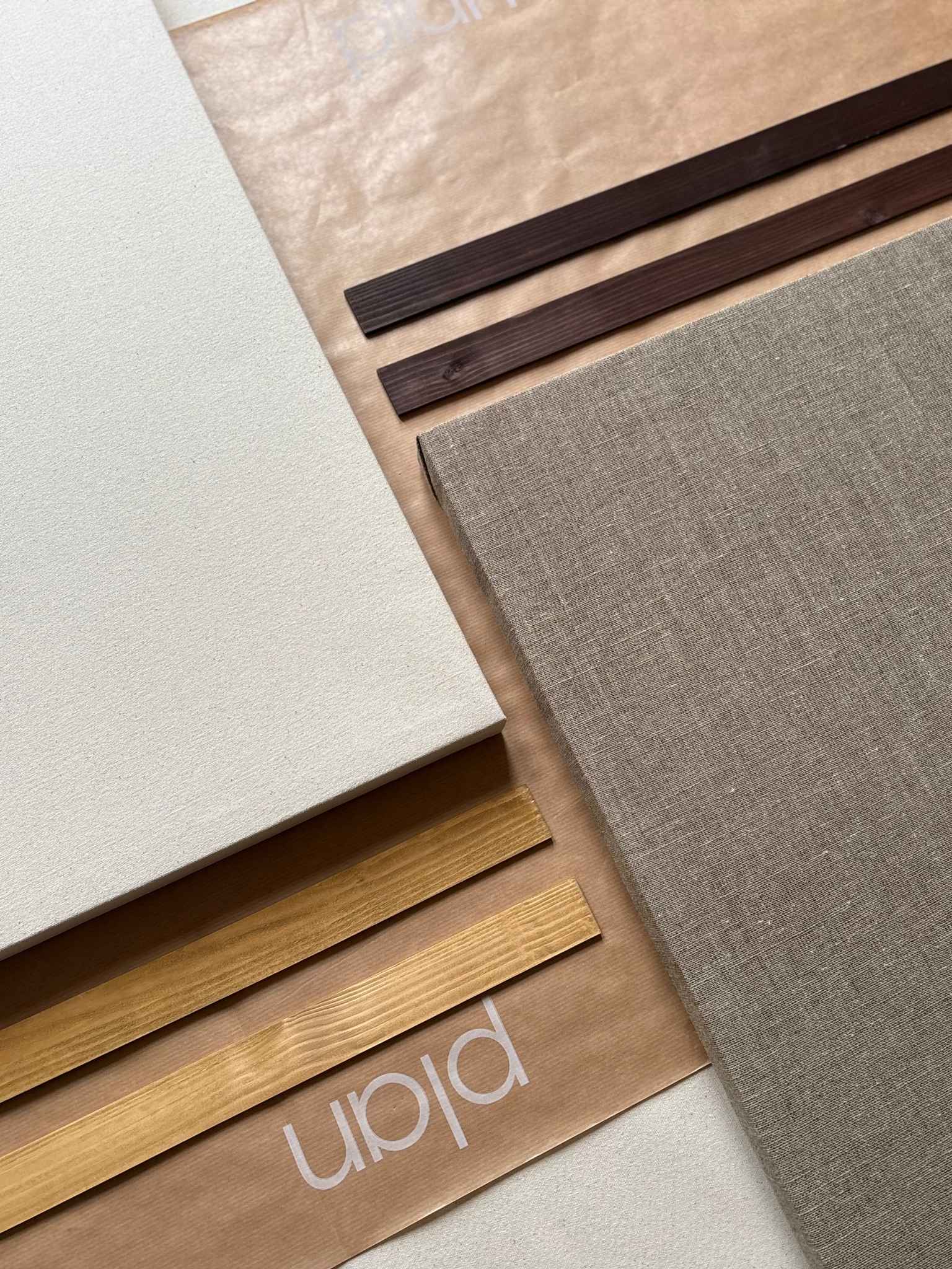 Flat lay of a blank framed canvas art kit showing cotton or linen canvas, solid wood edge frame bars, and Plan-branded packaging, highlighting the build-it-yourself frame system