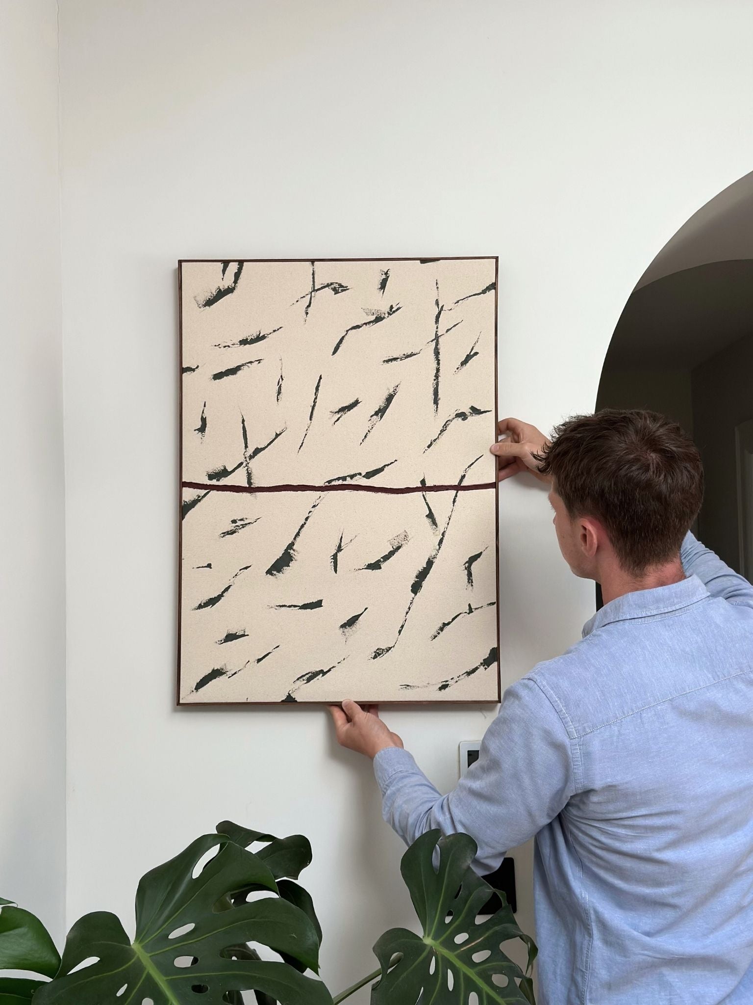 Finished abstract framed canvas art in forest red palette, handmade artwork from a DIY framed canvas art kit styled and being hung in a minimalist interior