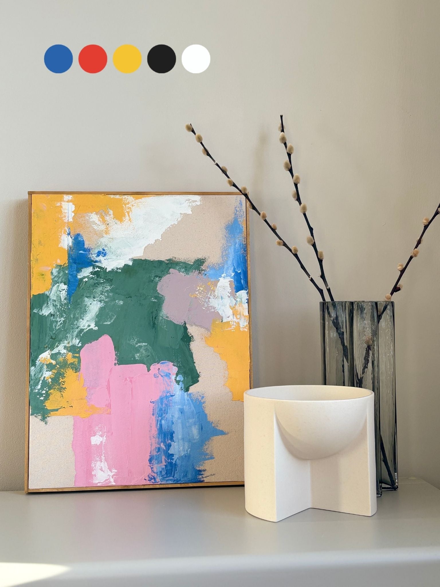 Colourful abstract framed canvas art created using primary paints, styled on a shelf with sculptural decor and dried branches, showcasing creative freedom and expressive mark-making.