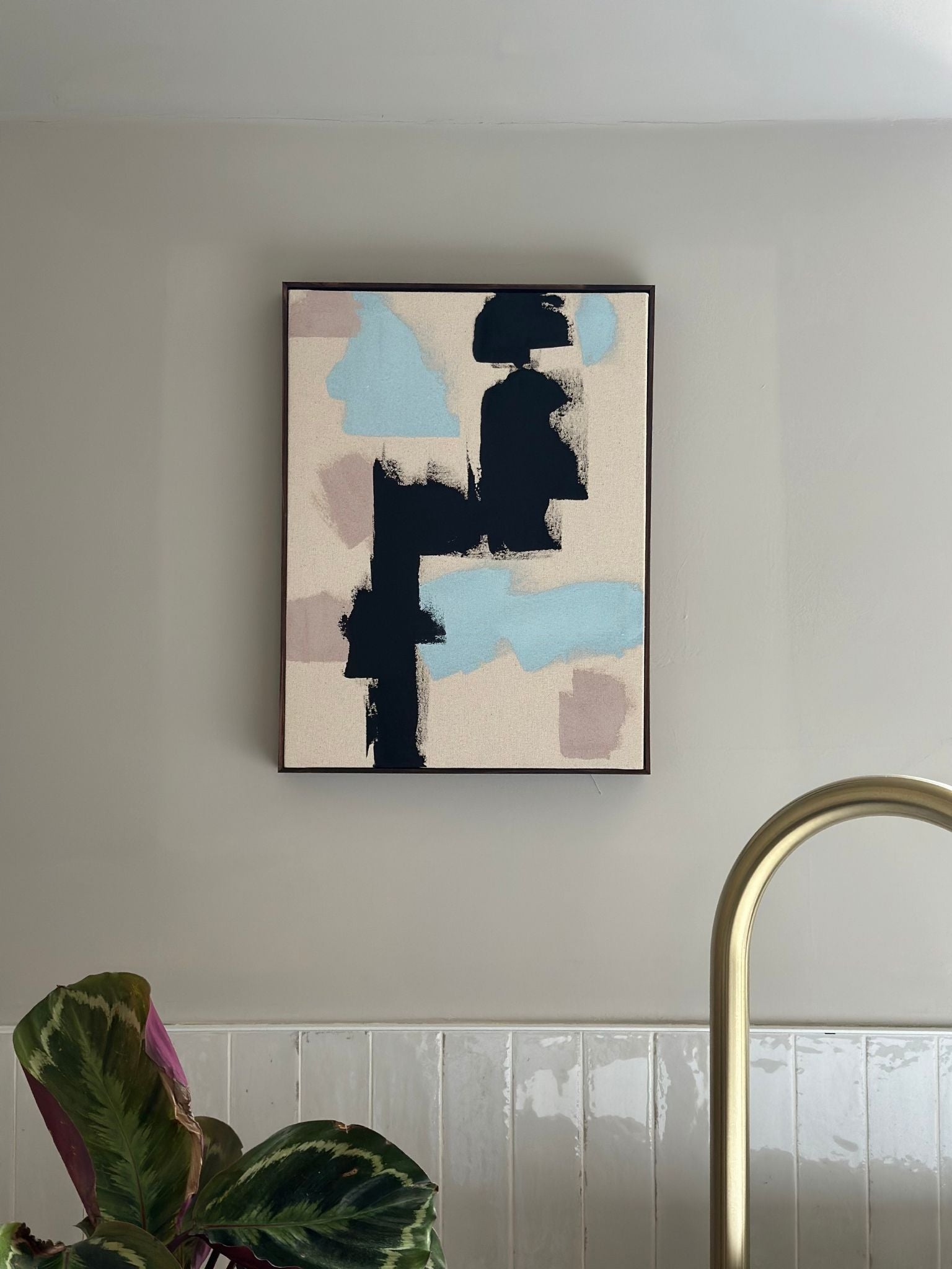 Abstract framed canvas artwork created with the Mix framed canvas art kit, featuring bold black brushstrokes with soft blue and neutral tones, styled on a light grey bathroom wall above a freestanding bath.