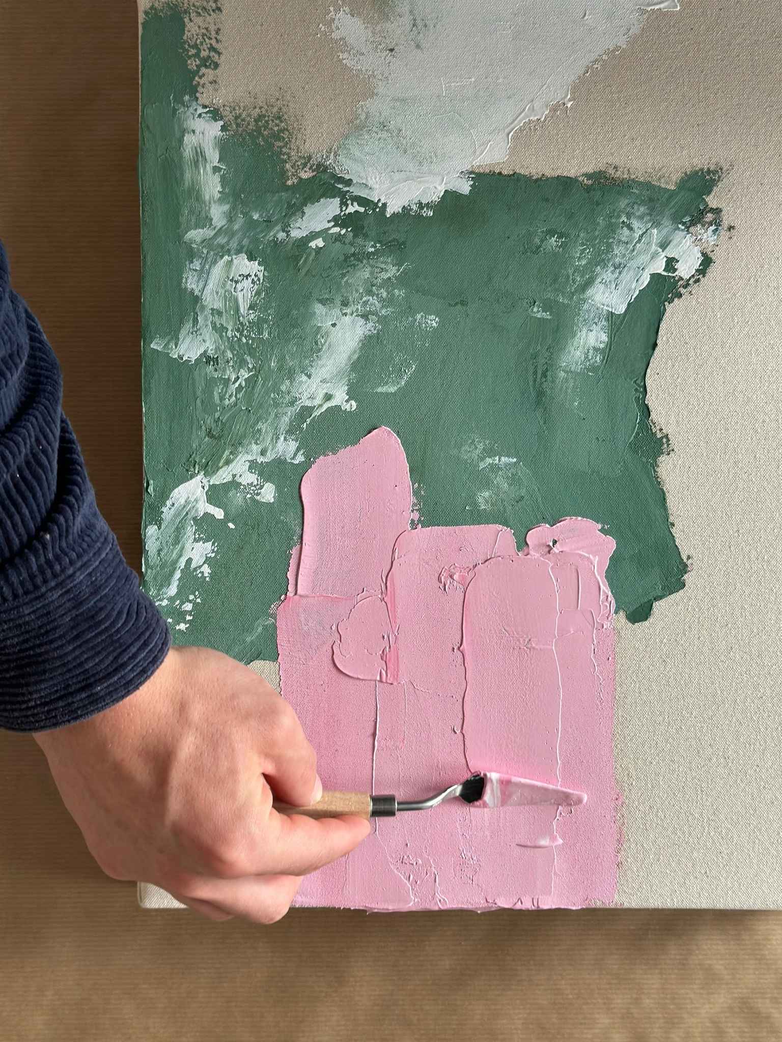 Close-up process shot of hand using a palette knife to spread pink acrylic paint onto canvas, demonstrating colour mixing and expressive texture with the Mix DIY framed canvas art kit.