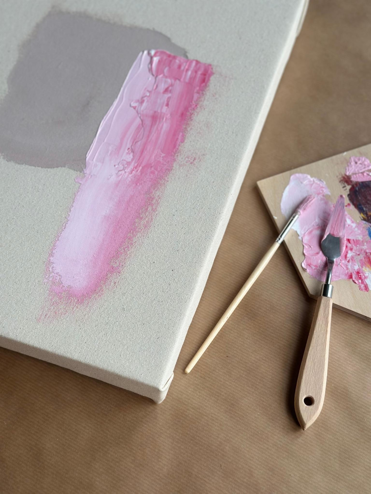 Close-up of colour mixing process on canvas, showing blended pink acrylic paint applied with palette knife, highlighting texture, brushstrokes and hands-on painting with a DIY framed canvas art kit.