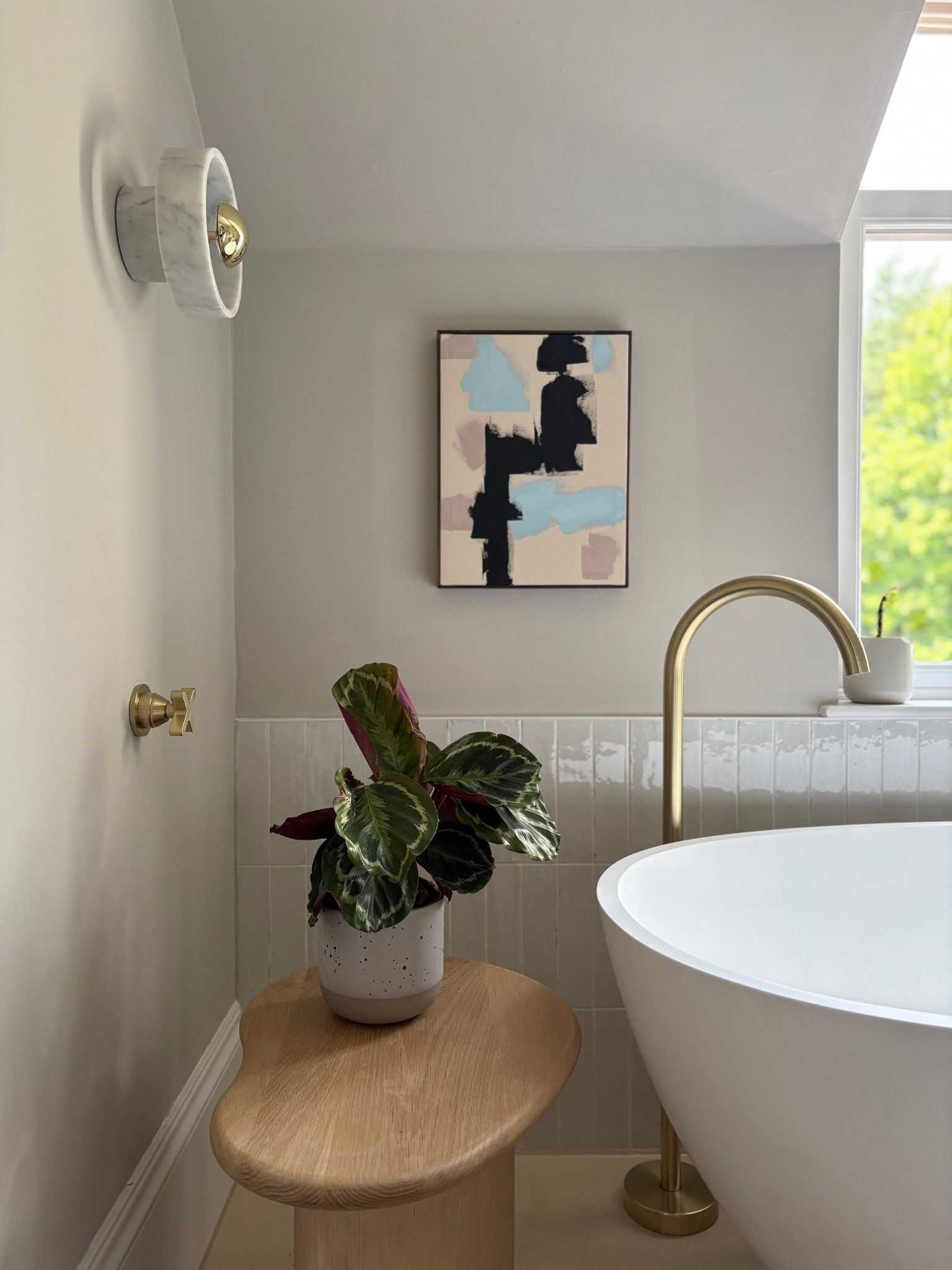 DIY abstract framed canvas art made using primary colours, styled in a modern bathroom with brass fittings, indoor plant and wooden stool, showcasing handmade wall art created at home.