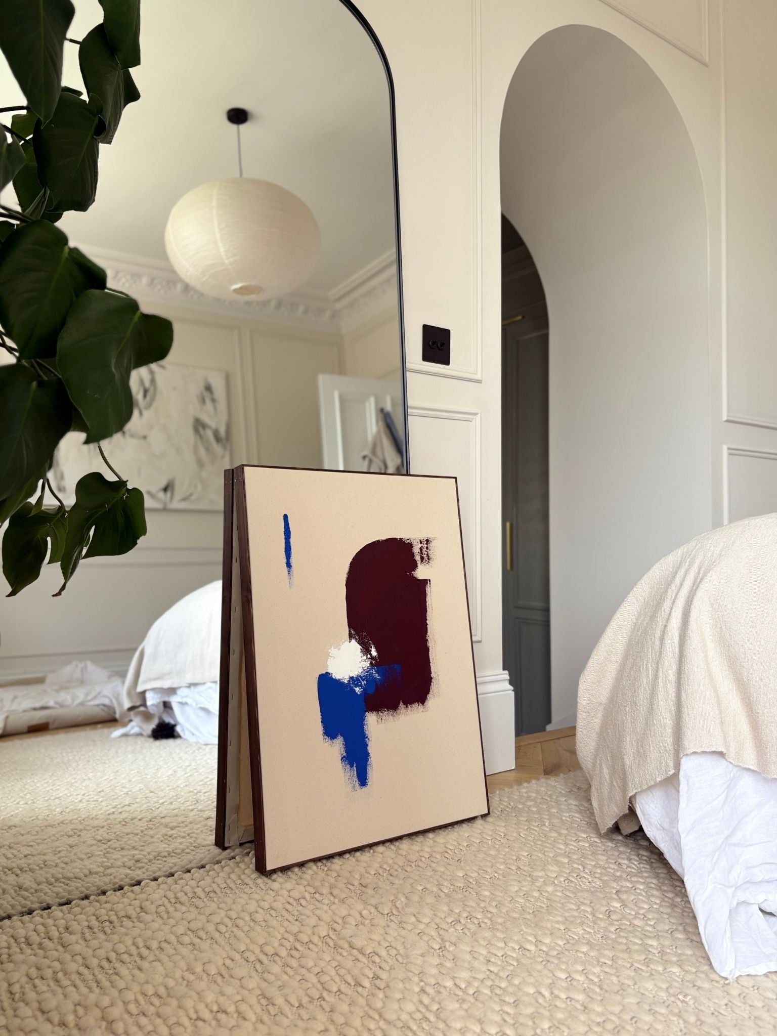 DIY framed canvas artwork created using primary colours, leaning against a mirror in a calm bedroom interior, showcasing abstract art made at home with a dark oak edge frame.