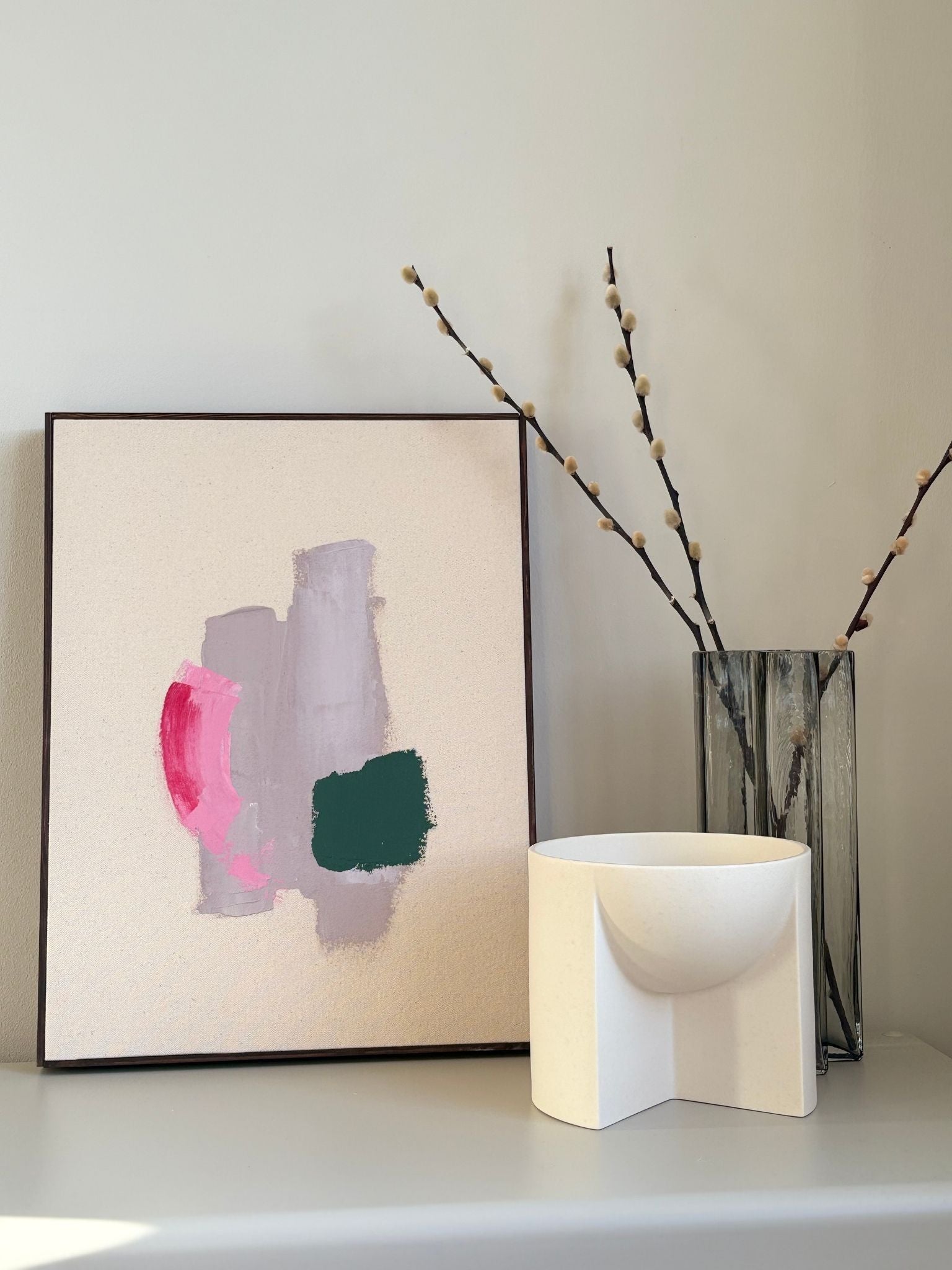 Abstract framed canvas artwork created by freely mixing primary colours, featuring soft pink, green and neutral brushstrokes, styled on a shelf as modern handmade wall art.