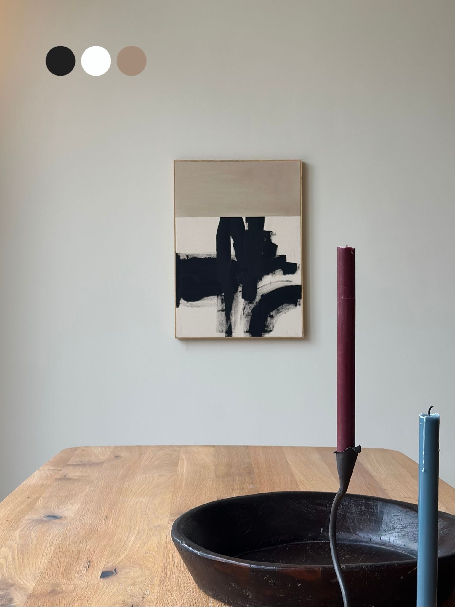Monochrome abstract framed canvas artwork featuring expressive black brushstrokes on beige cotton canvas, styled in a calm dining space with candles and wooden furniture.