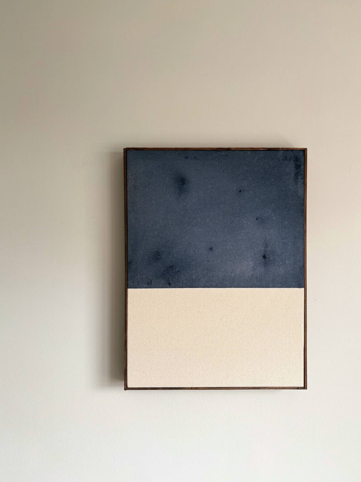 A minimalist framed wall art piece hanging on a light beige wall, featuring a horizontal split design with a dark navy blue textured top half and a warm cream bottom half.