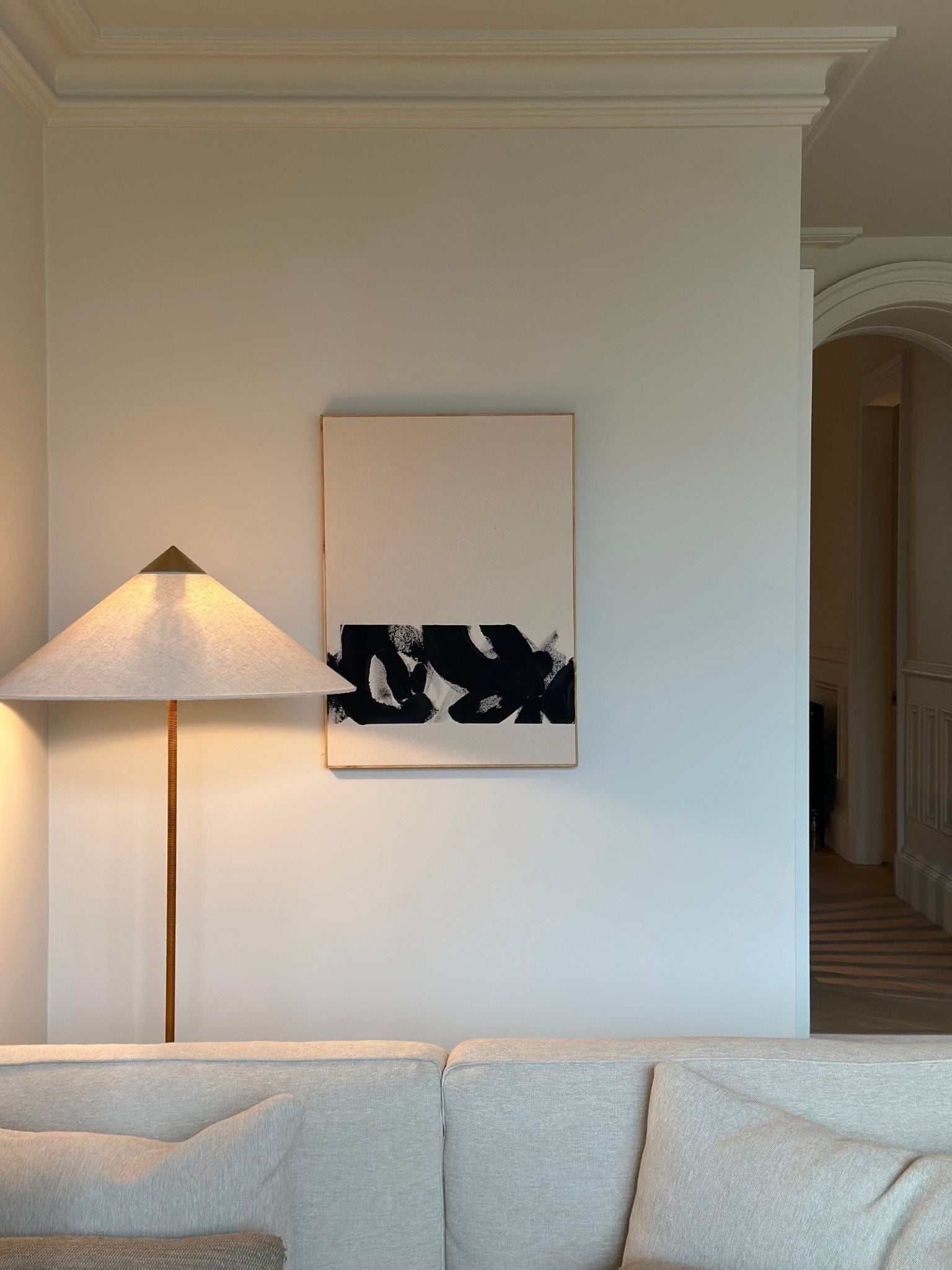 Monochrome abstract framed canvas artwork created with the cotton framed canvas art kit by Plan, featuring bold black brushstrokes on beige cotton canvas, styled on a living room wall above a sofa with a floor lamp.