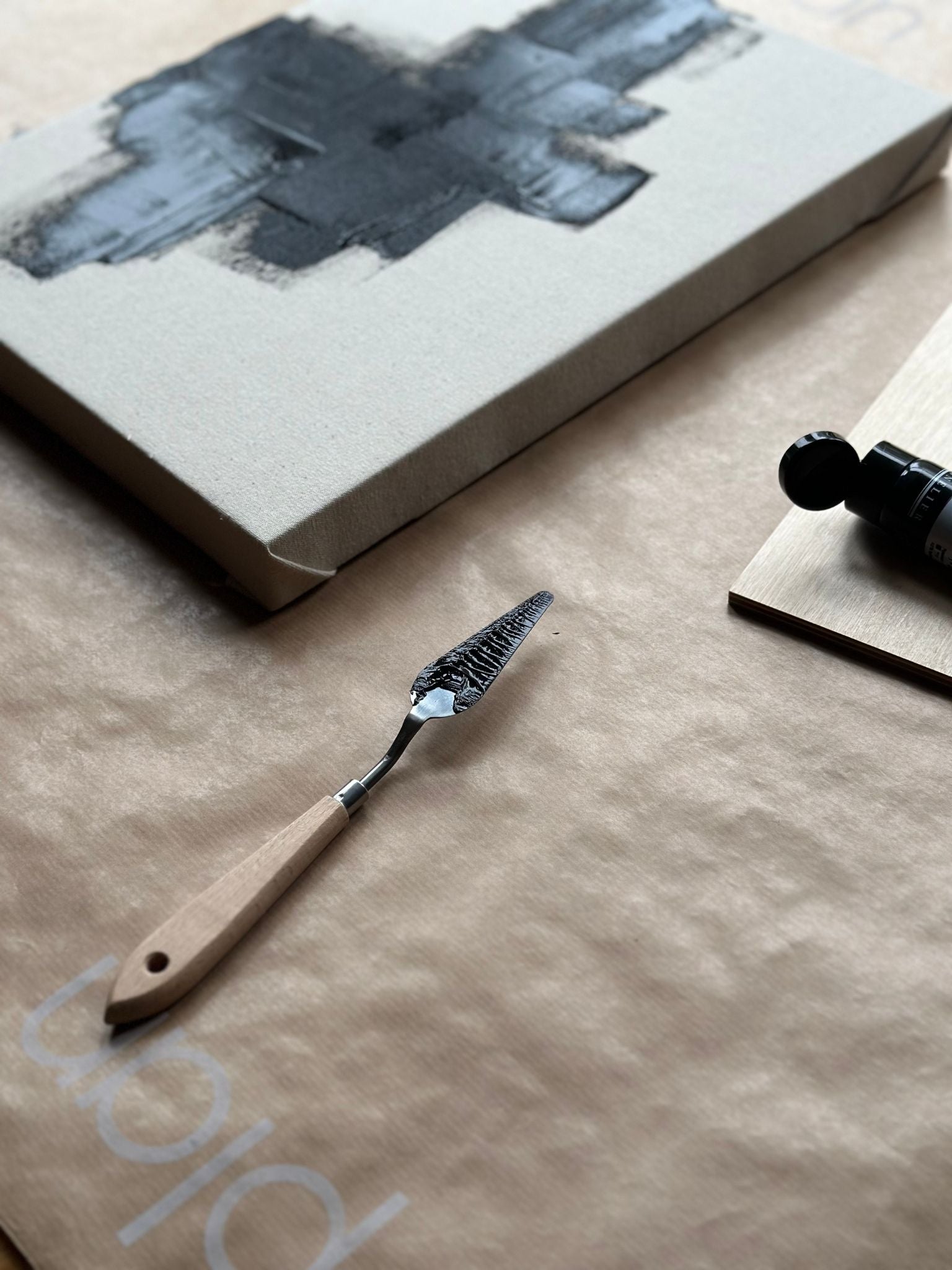 Detail process shot of black acrylic paint spread across cotton canvas with a palette knife, showing layered texture and raw canvas surface.