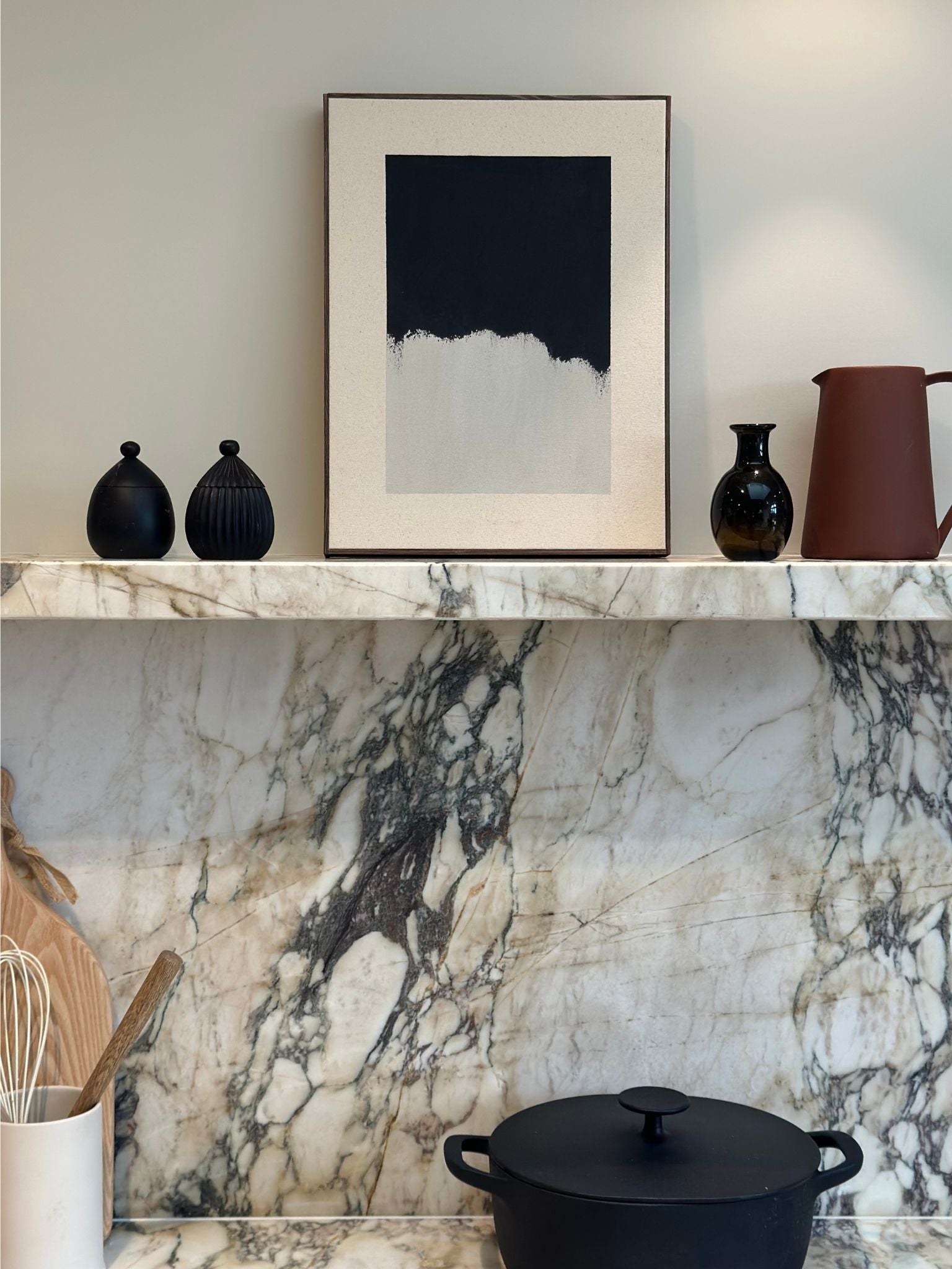Minimal monochrome framed canvas artwork featuring black brushstrokes on beige cotton canvas, styled on a marble kitchen shelf with ceramic vessels and cookware.