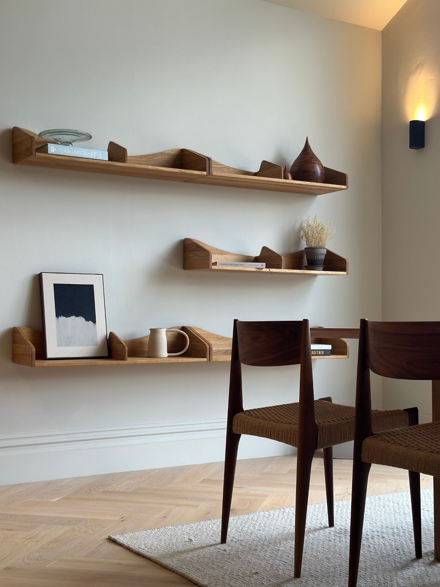 Monochrome abstract framed canvas art displayed on wooden wall shelves in a dining space, featuring black and white paint on beige cotton canvas with minimalist interior styling.