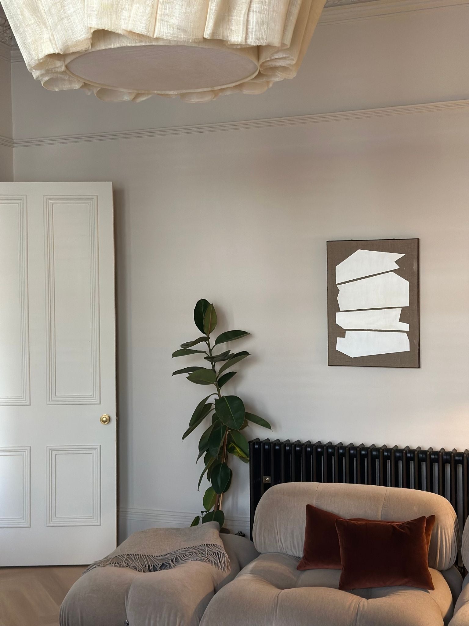 Monochrome framed linen canvas artwork displayed in a living room setting, featuring white geometric shapes on raw linen canvas, styled above a radiator beside a sofa and indoor plant.