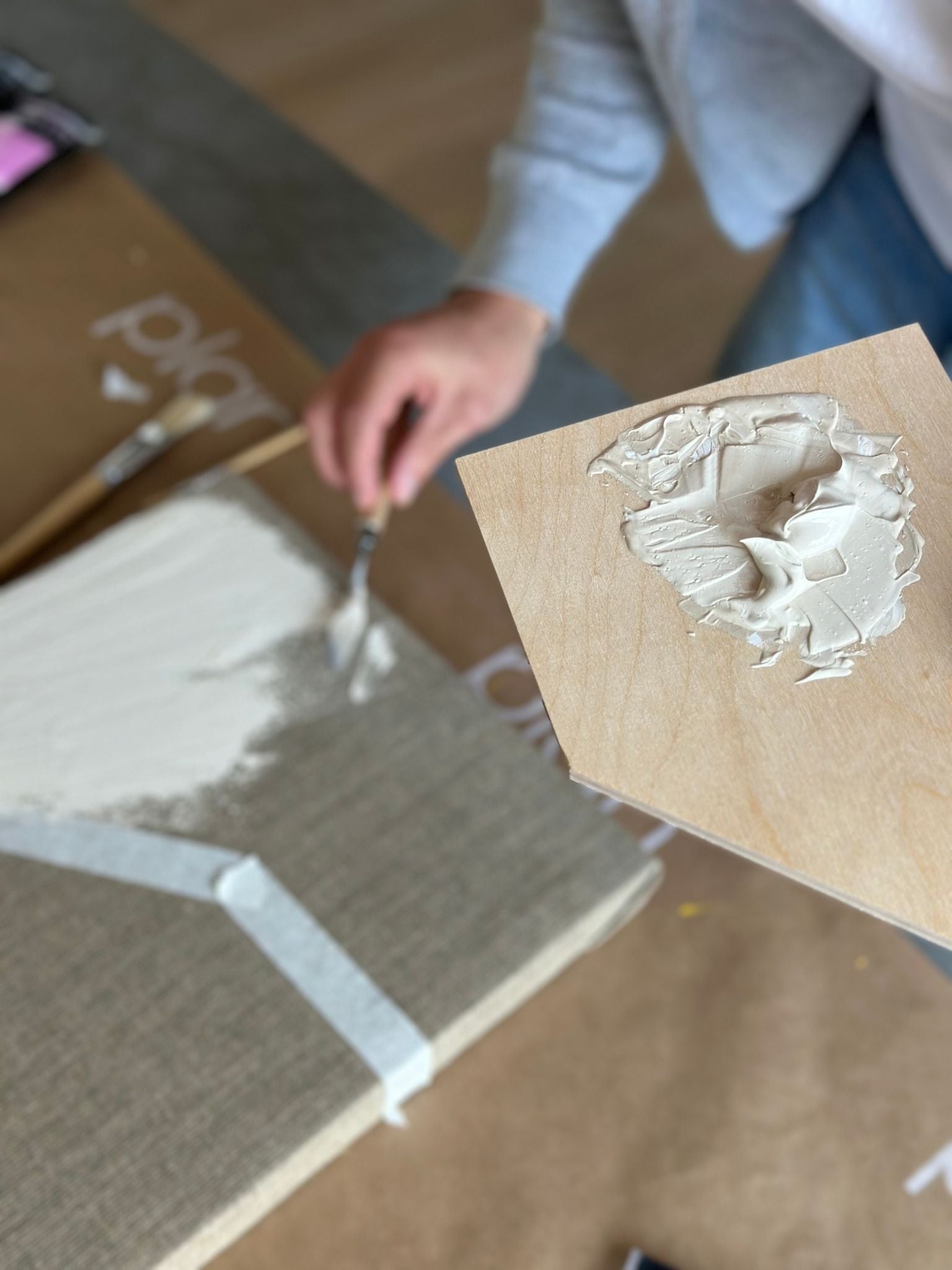 Process shot of monochrome linen framed canvas art kit with beige acrylic paint mixed on a wooden palette and applied to raw linen canvas