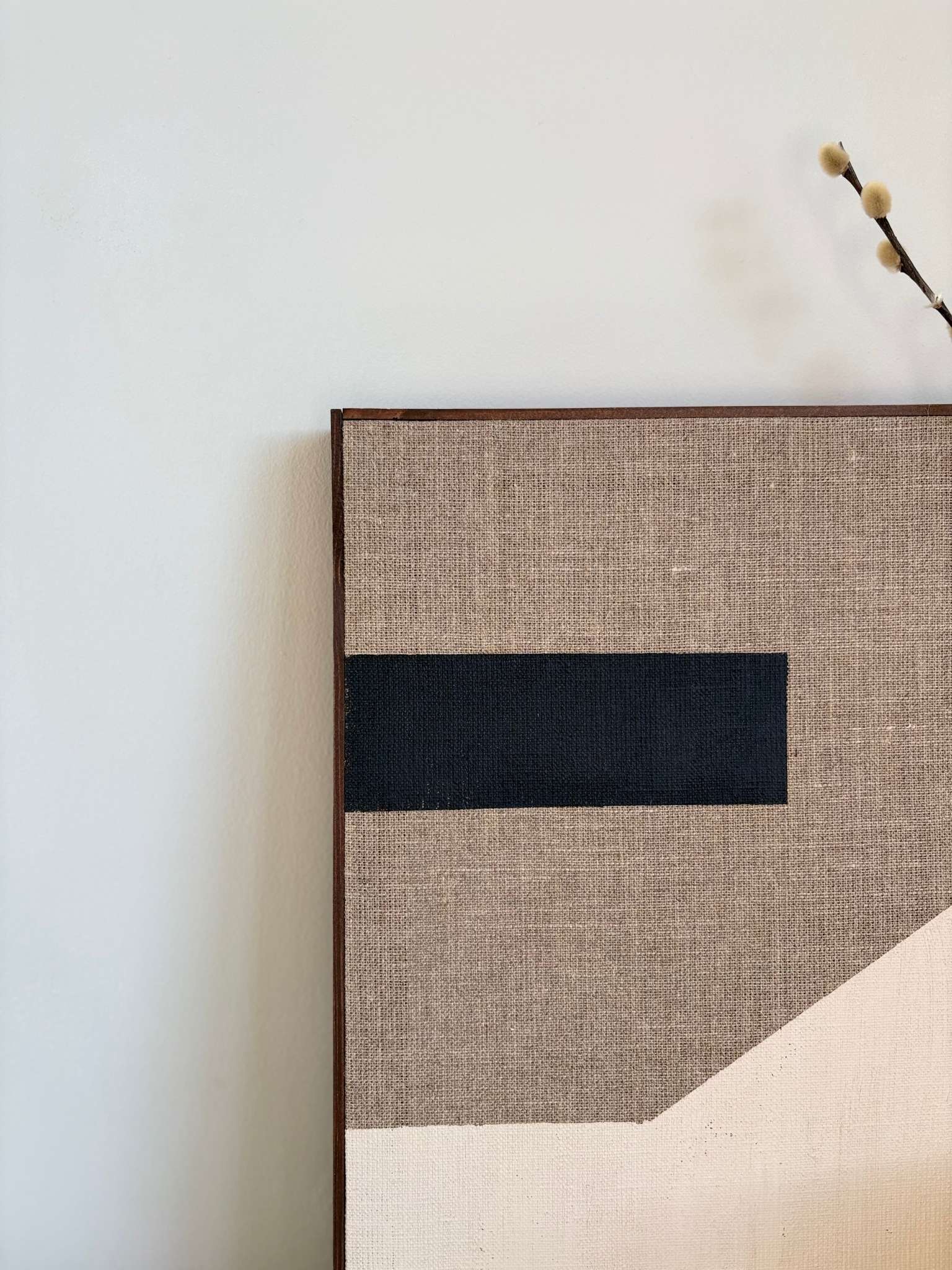 Close-up of monochrome framed canvas art on linen, featuring a bold black horizontal brushstroke on raw linen canvas with beige geometric detailing.