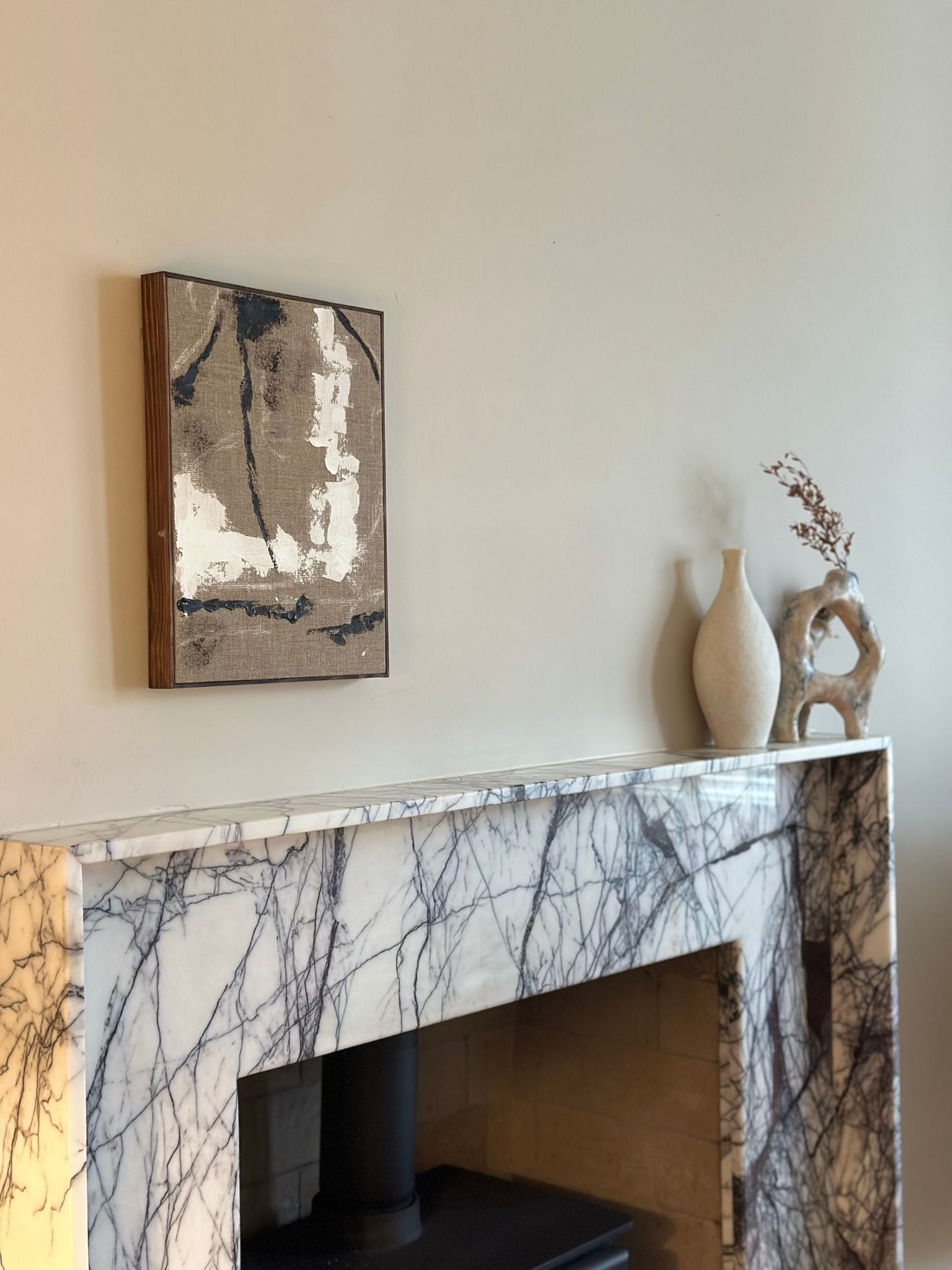 Framed monochrome linen canvas art shown hanging above a marble fireplace, featuring expressive black and white abstract brushstrokes in a minimalist interior.