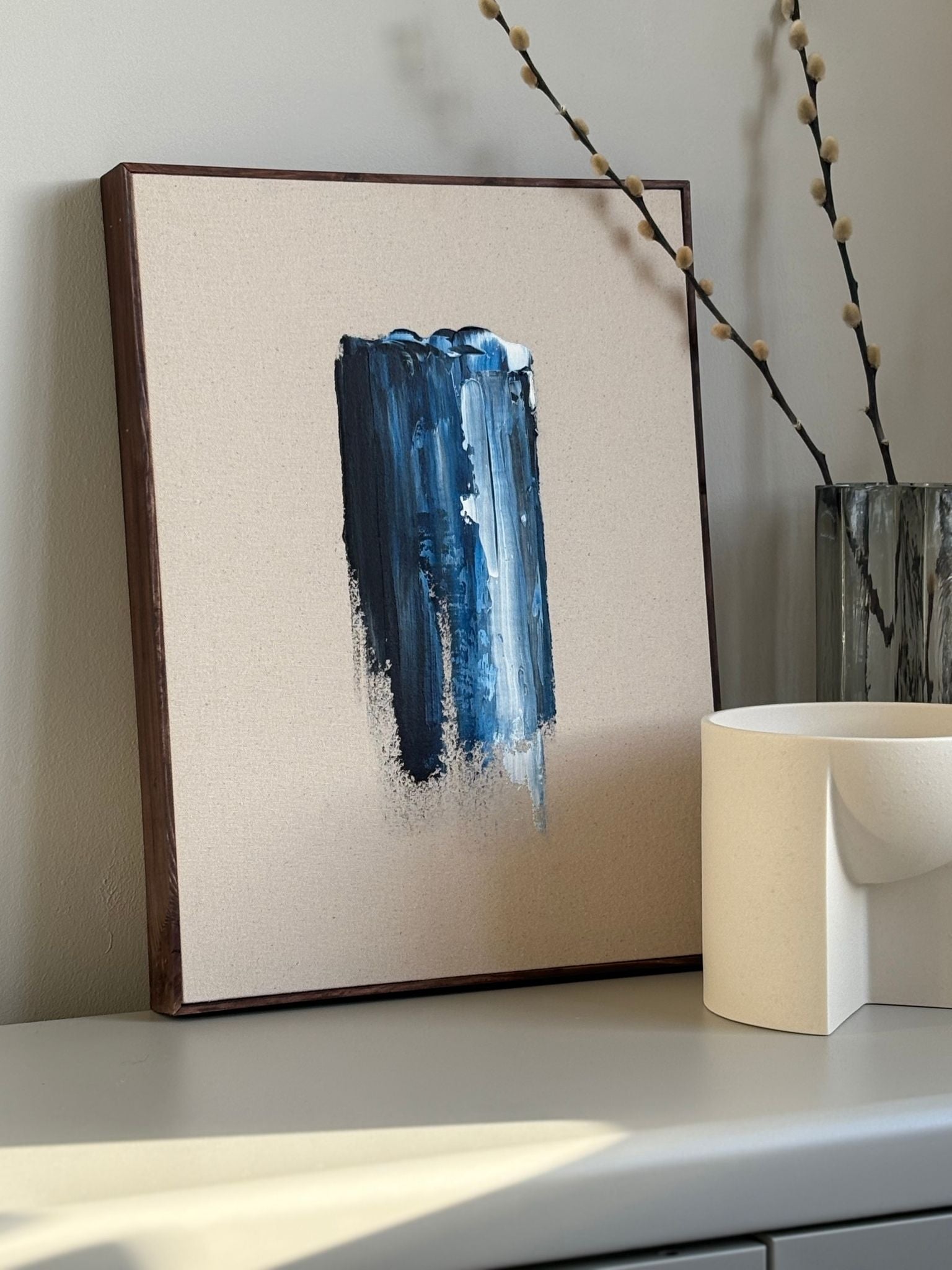 Abstract framed canvas artwork created with the Navy & Bright framed canvas art kit, featuring vertical navy and light blue brushstrokes on raw canvas, styled on a shelf beside minimalist decor.