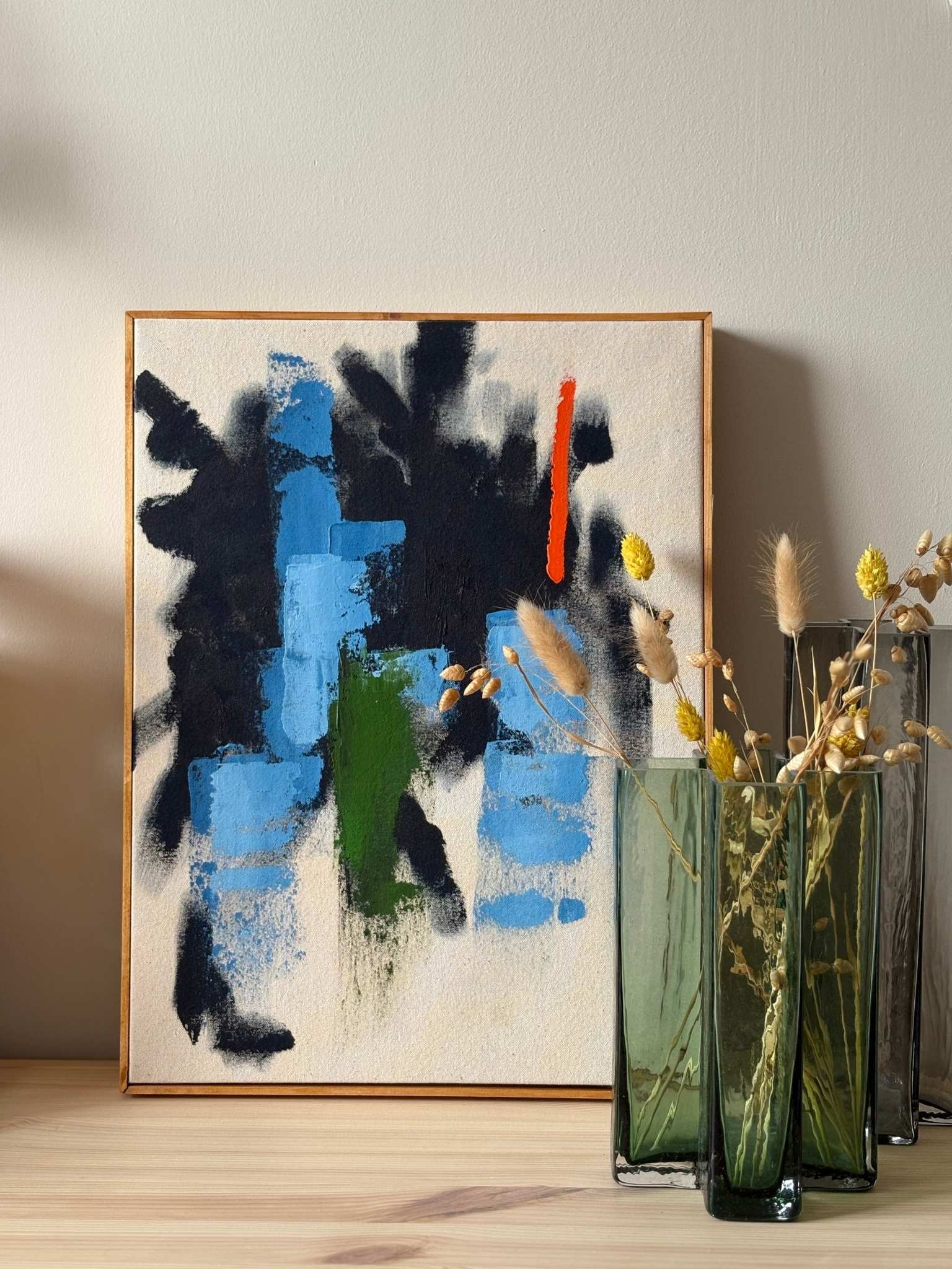 Bold abstract framed canvas artwork made with navy and bright accent colours, styled on a wooden surface with glass vases and dried flowers for home decor inspiration.