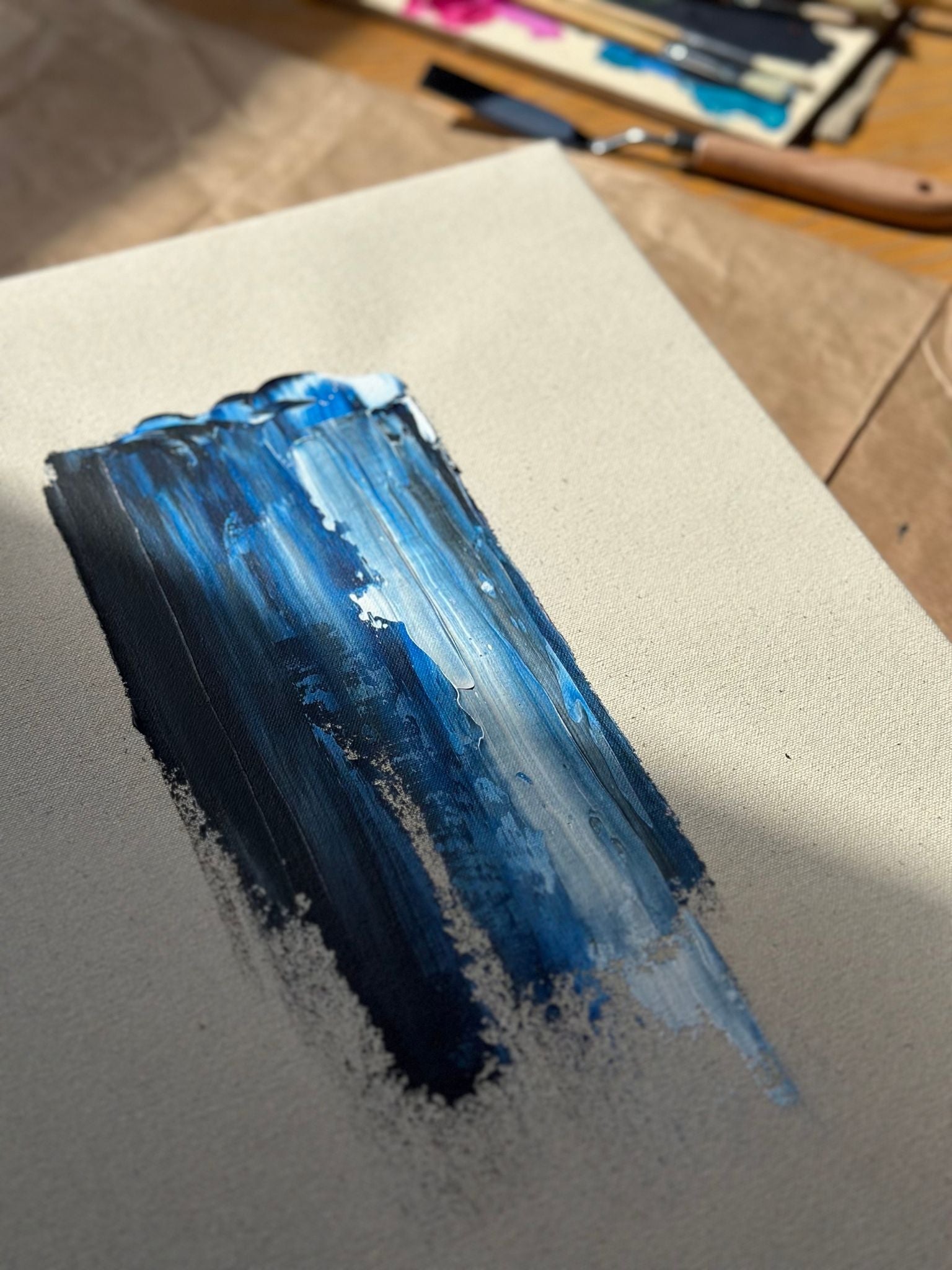 Close-up process shot of abstract painting in progress using the Navy & Bright canvas art kit, showing layered navy and light blue acrylic paint applied vertically on raw canvas.