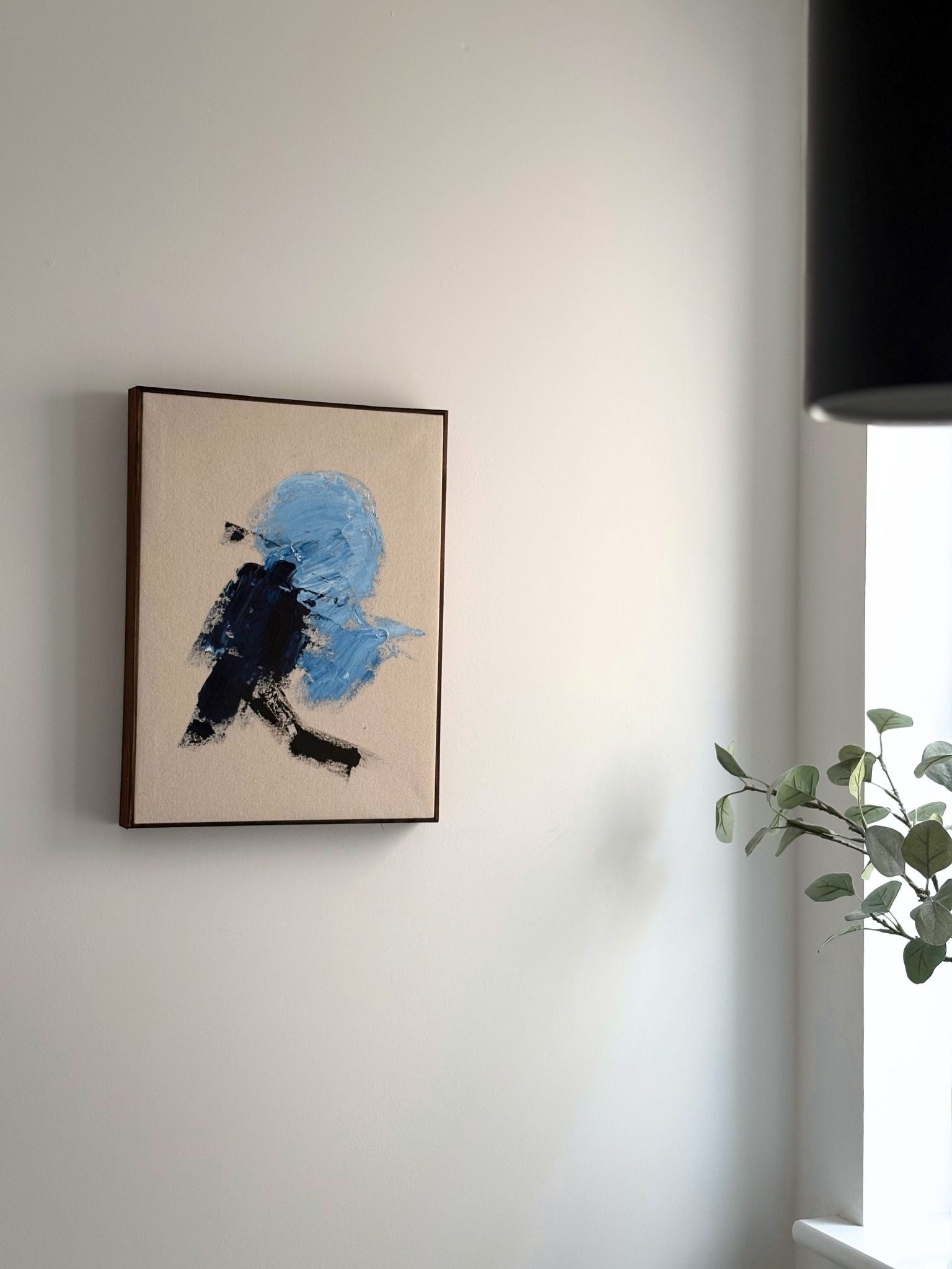 Minimal abstract framed canvas art created using the Navy & Bright palette by Plan Art, featuring black and light blue brushstrokes, styled on a white wall with natural light.