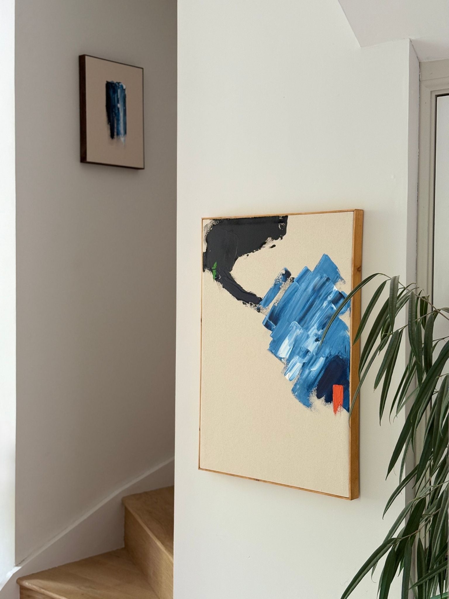 Abstract framed canvas art made using navy and bright colour accents, styled in a hallway setting with staircase and indoor plant, showcasing modern handmade wall art.