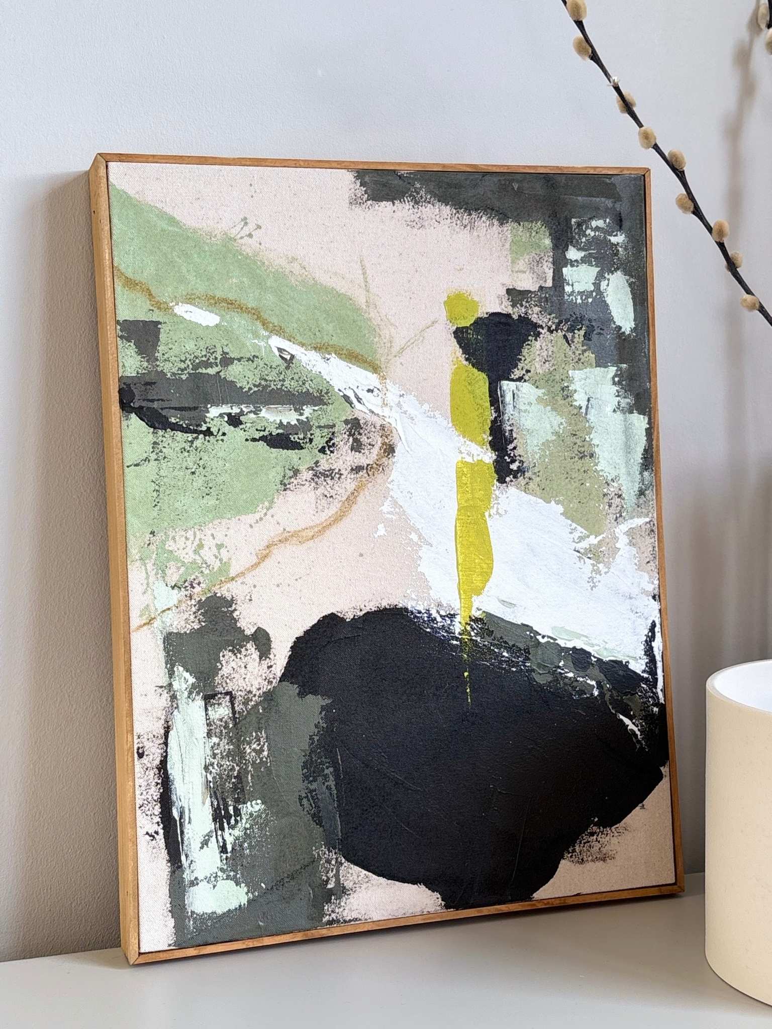 Framed olive abstract artwork on cotton canvas, styled on a shelf beside a vase and decorative branch in a calm, minimalist interior