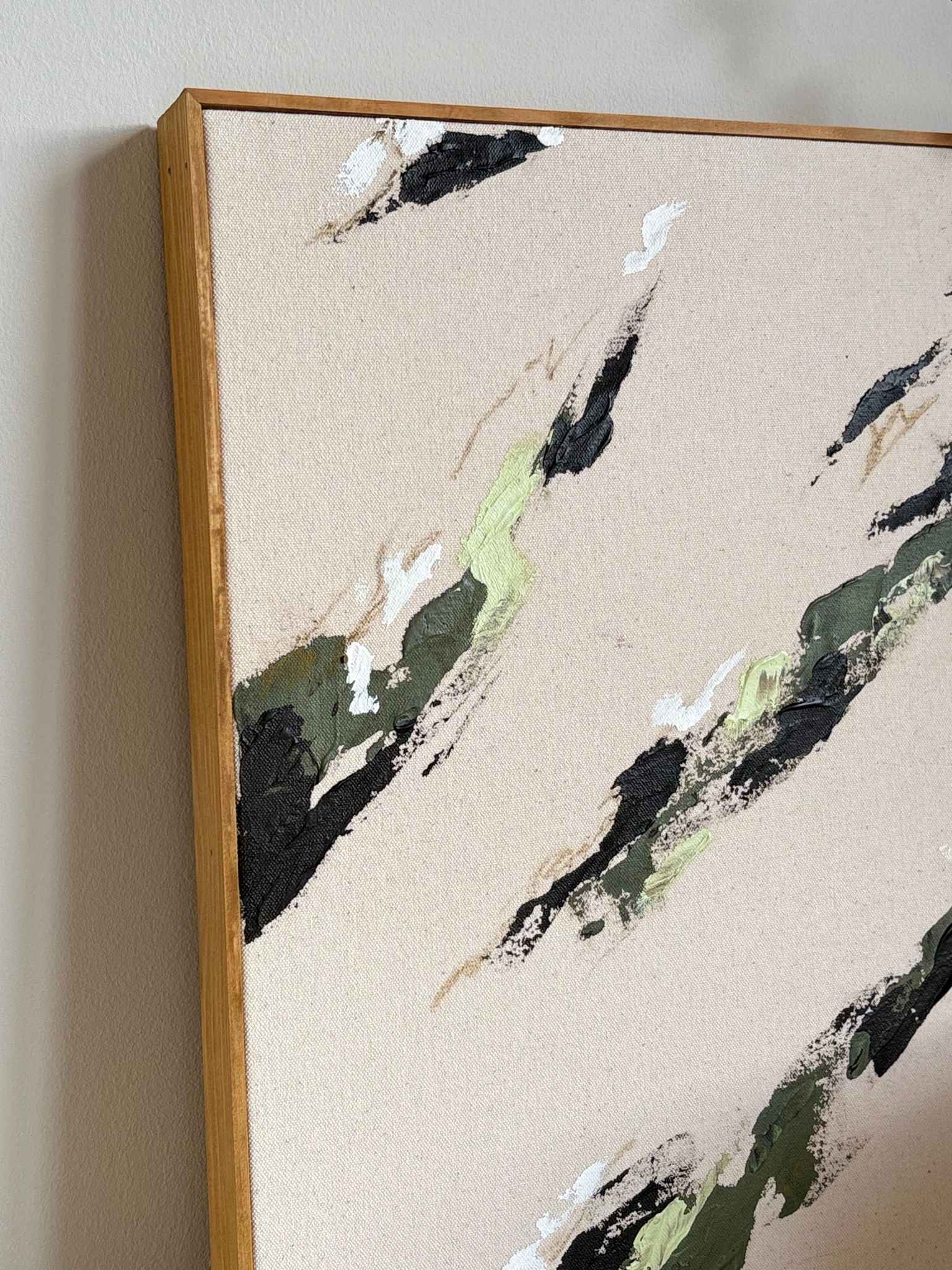 Close-up of a framed olive abstract artwork on natural cotton canvas, showing textured green, black and white brush marks within a slim handcrafted oak frame