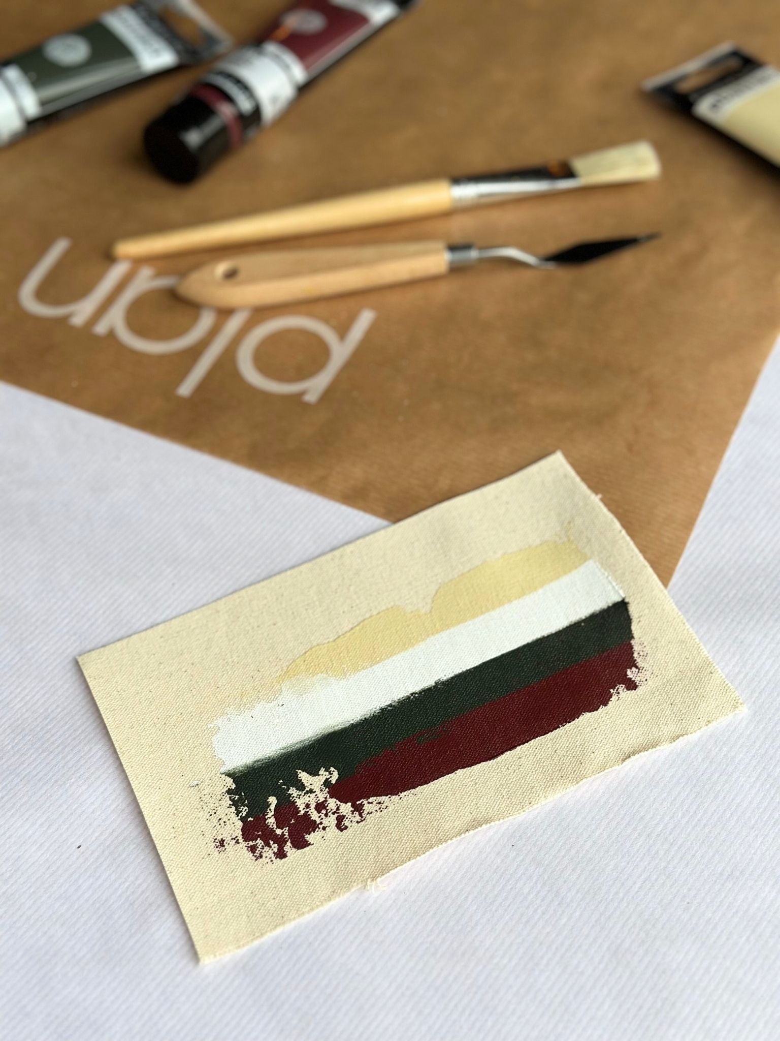 Red and green colour palette swatch for Plan DIY framed canvas art kit, featuring deep green, red, beige and white acrylic paint on natural cotton canvas