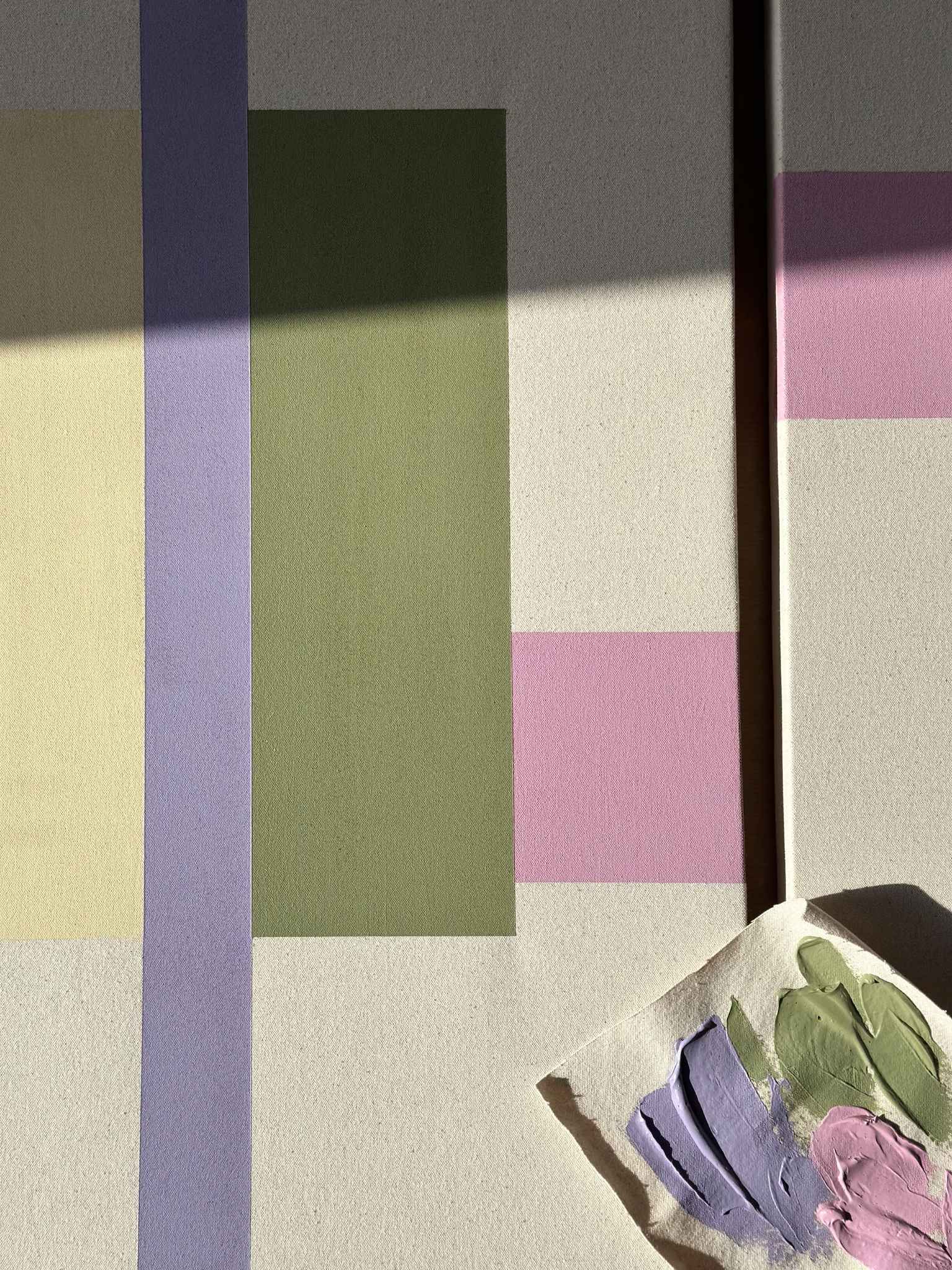 Close-up of two abstract framed canvas artworks with soft pastel colour blocks and the painting process with a canvas practice piece and acrylic paints mixed using primary colours, DIY wall art made at home