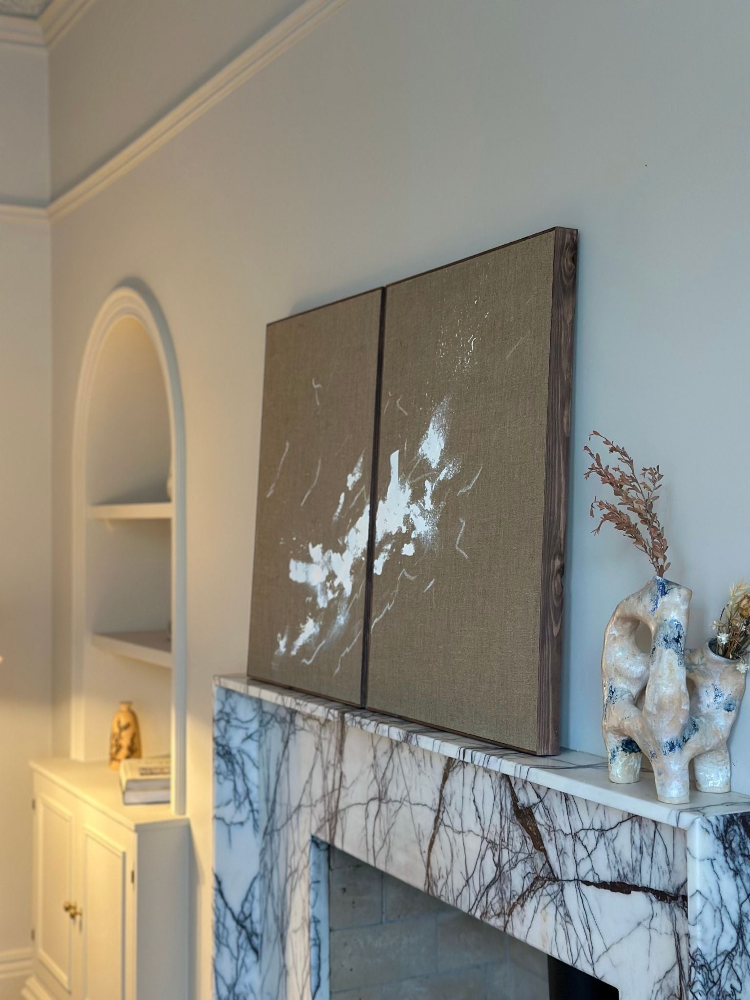 Monochrome linen framed canvas artworks with dark oak edge frame styled on a marble fireplace with sculptural decor and neutral tones