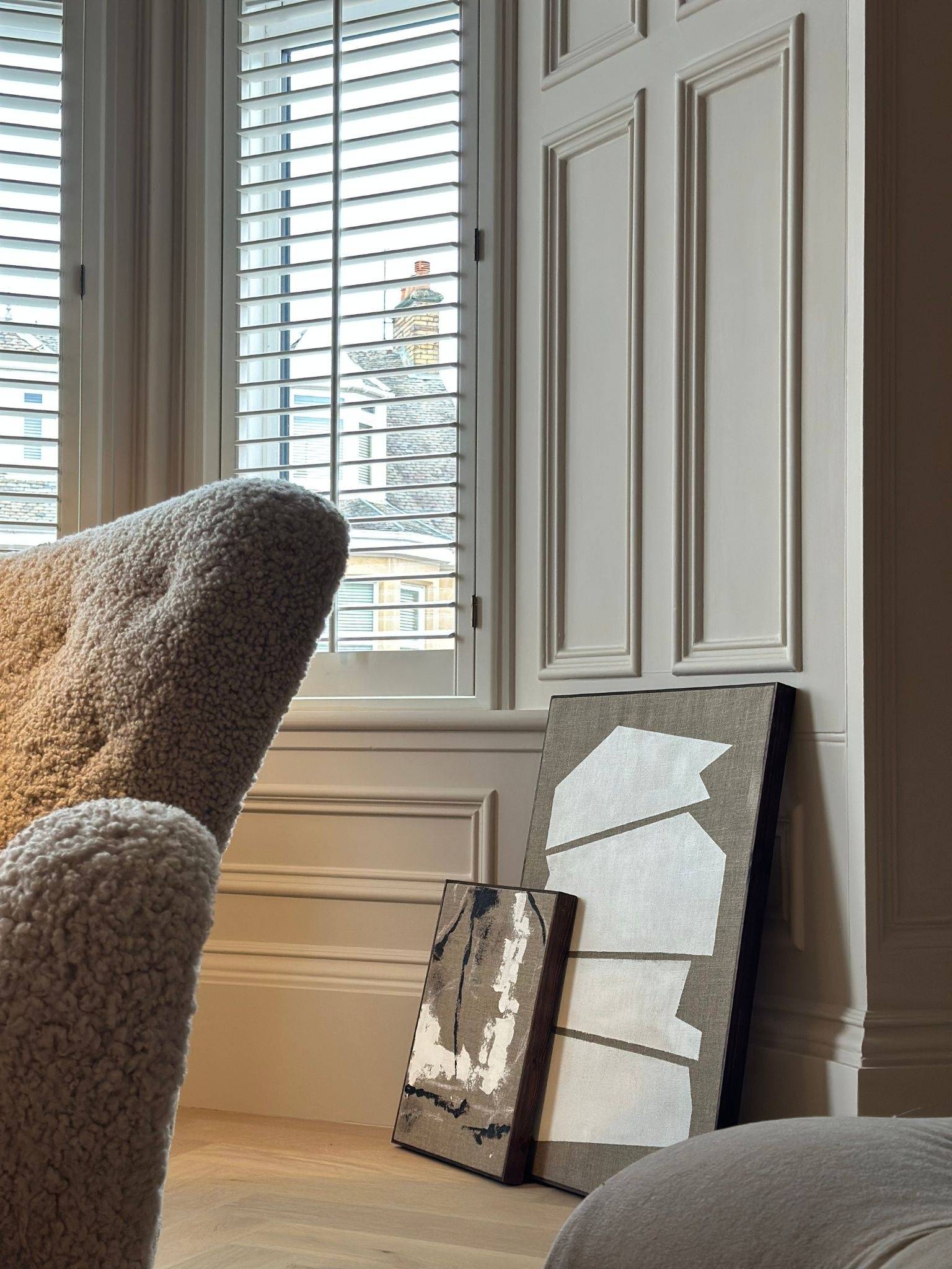 Monochrome framed canvas artworks leaning against the wall near a window, showcasing white abstract shapes on raw linen