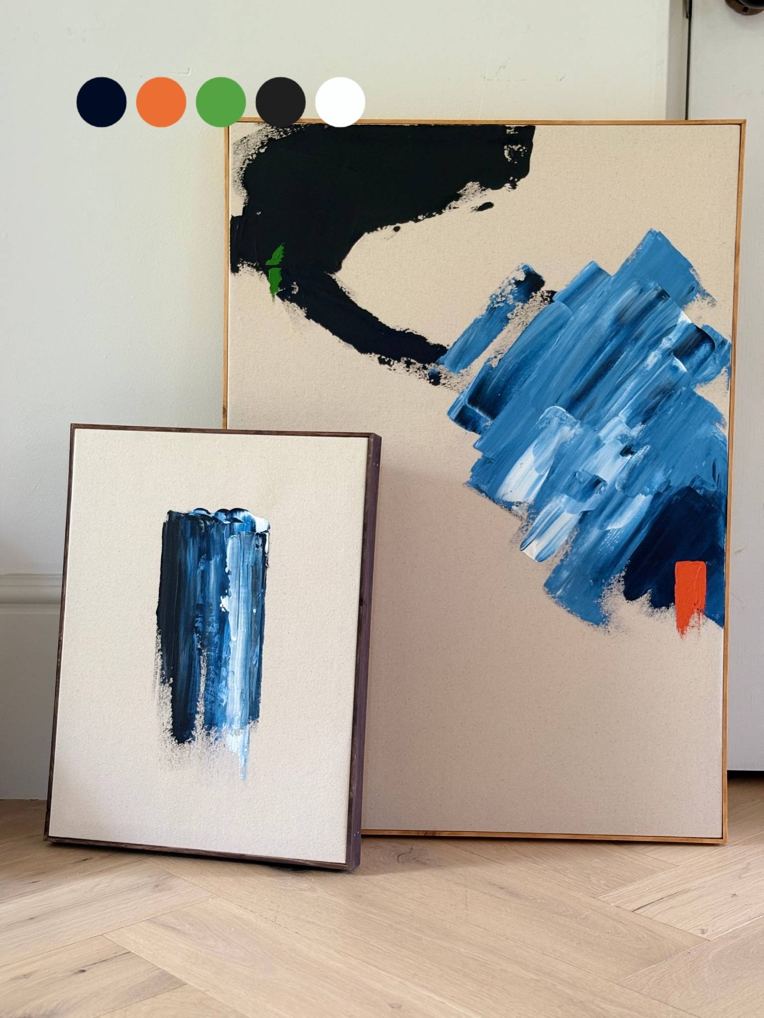 Two finished abstract artworks created with the Navy & Bright double framed canvas art kit, shown side by side on the floor, featuring bold blue, black and accent colour brushstrokes on raw cotton canvas with handcrafted oak and dark oak edge frames.