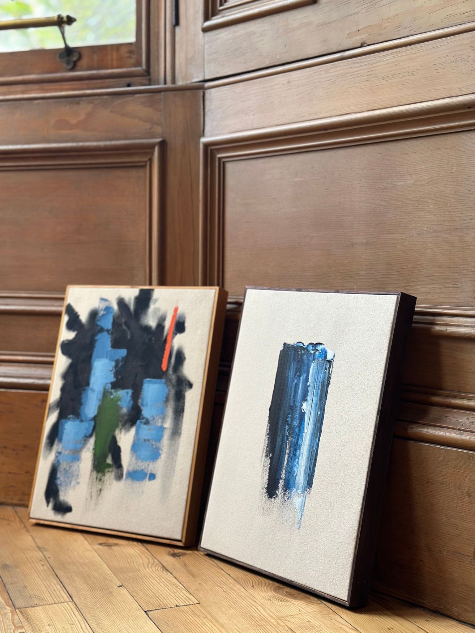 Lifestyle image of two finished abstract paintings made with the Navy & Bright double framed canvas art kit, featuring bold navy blue marks, bright accent details and locally handcrafted wooden frames.